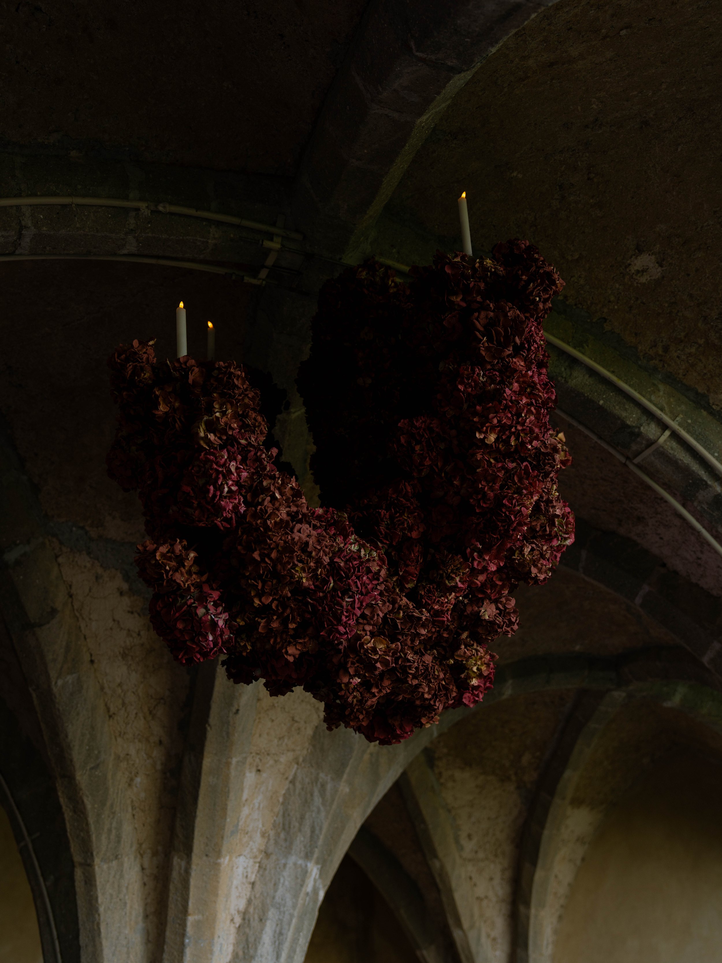 A dark, arched stone ceiling with two lit candles in front of a floral arrangement.