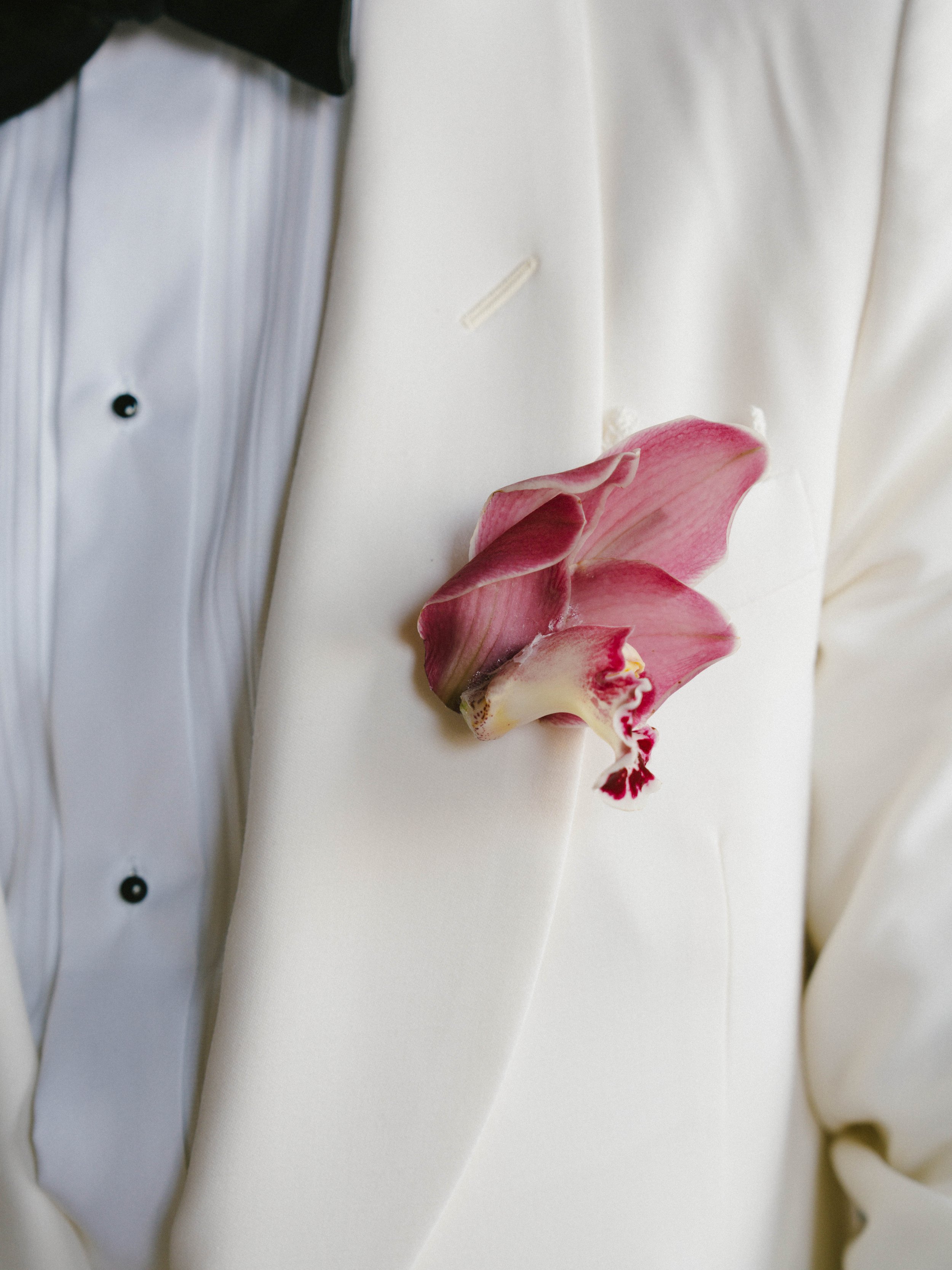 Close-up of a pink and white orchid flower pinned to a white tuxedo jacket worn over a white shirt with black buttons. Villa Cimbrone wedding Amalfi Coast