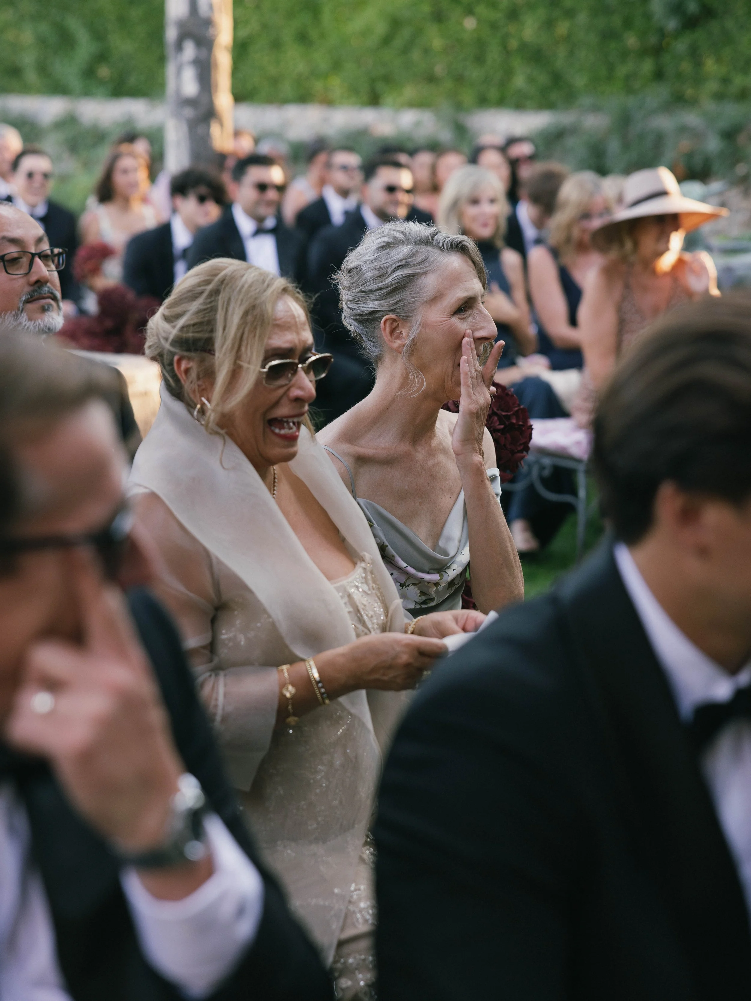 An outdoor wedding ceremony with emotional guests, including women in elegant dresses and men in tuxedos, watching the event. Villa Cimbrone wedding Amalfi Coast
