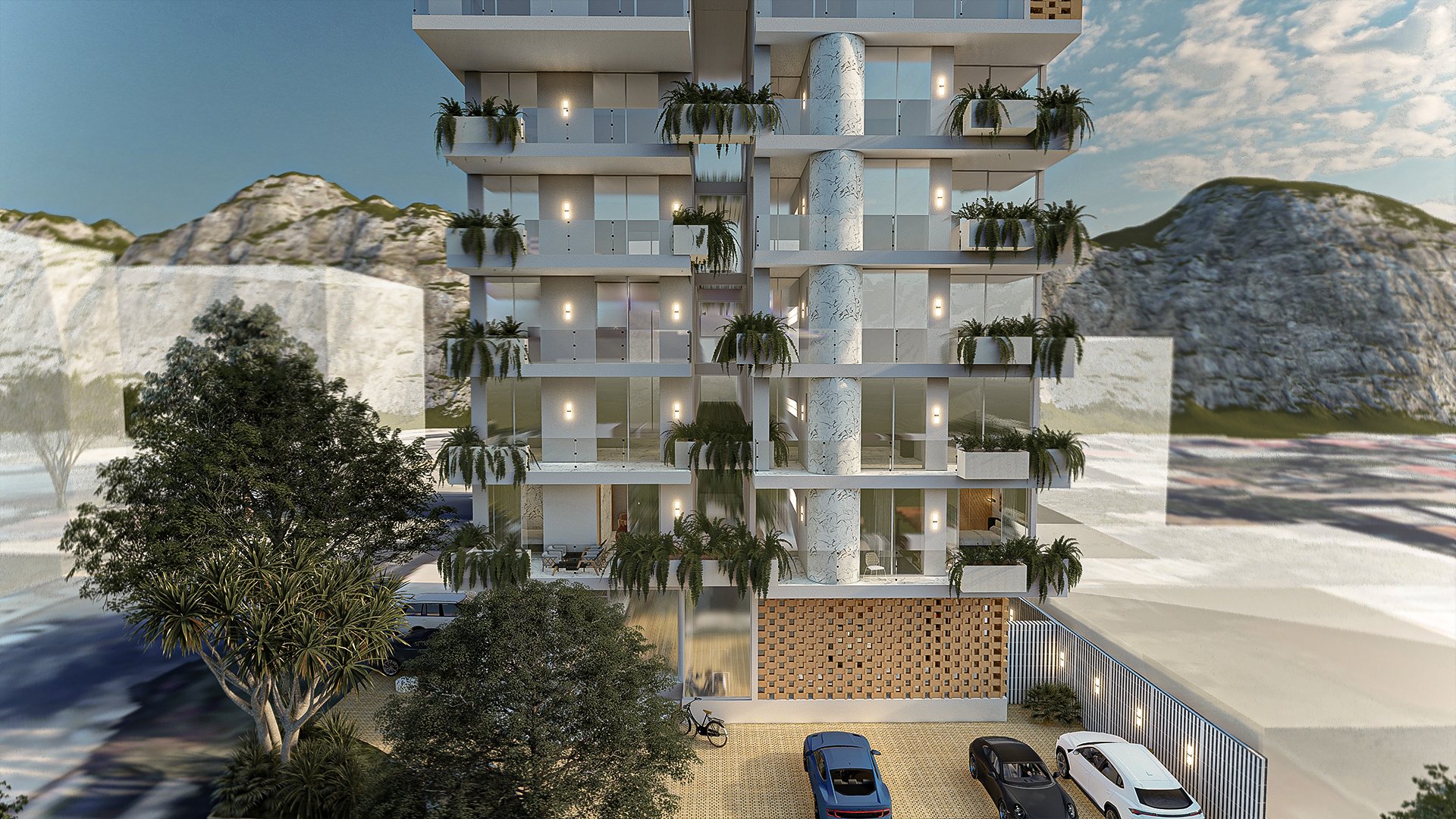 Edificio moderno con balcones y plantas, rodeado de montañas, árboles y varios coches estacionados en el frente.