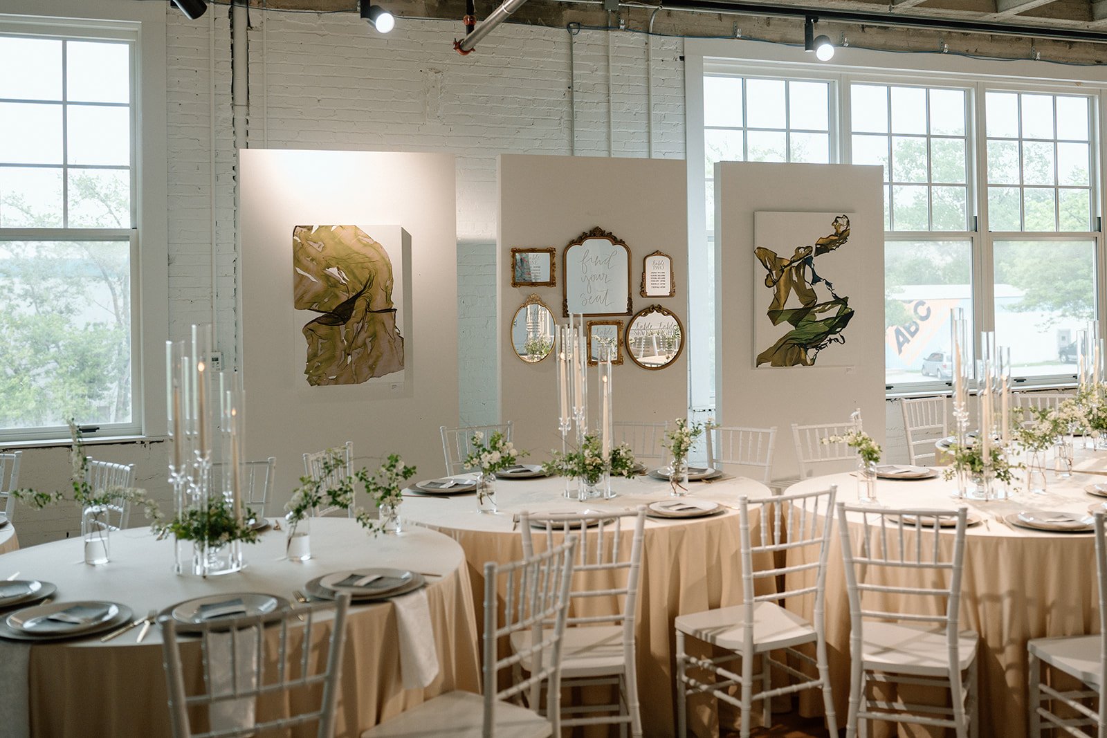 Spacious contemporary gallery room at Zhou B Art Center Kansas City with large windows providing natural light, polished wood floors, exposed industrial ceilings, lounge seating, and modern artworks displayed on movable white panels and walls.
