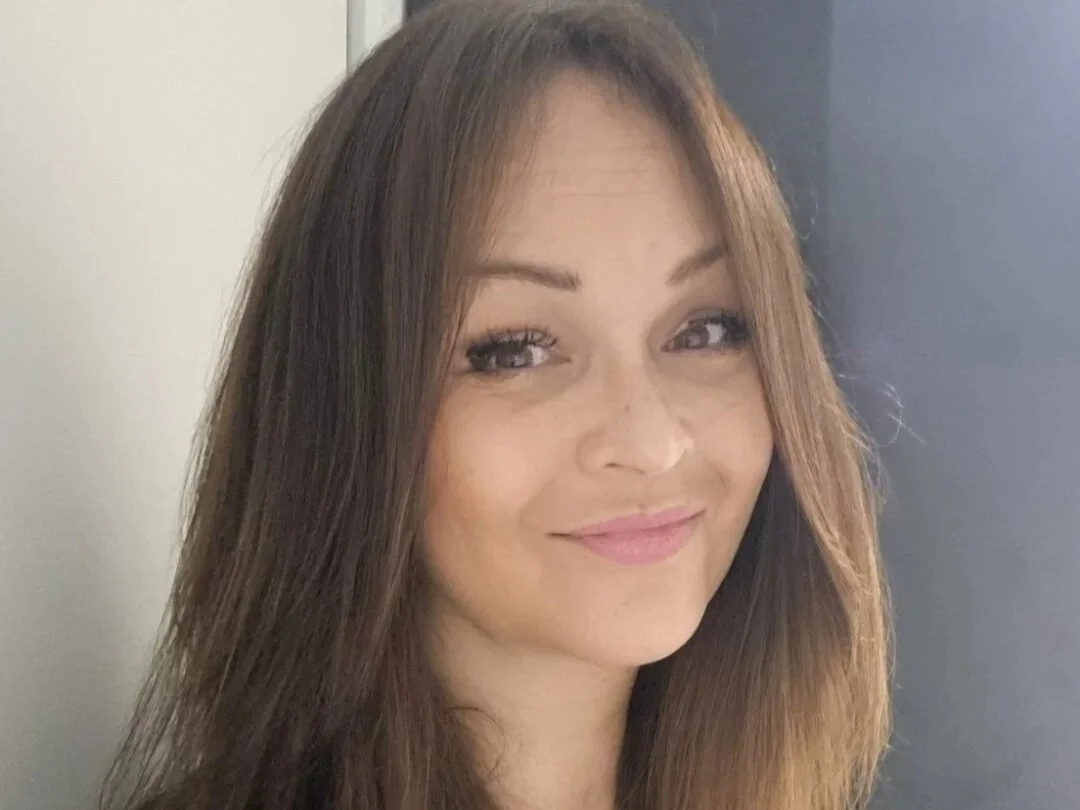A woman with long brown hair, light makeup, smiling and looking at the camera.