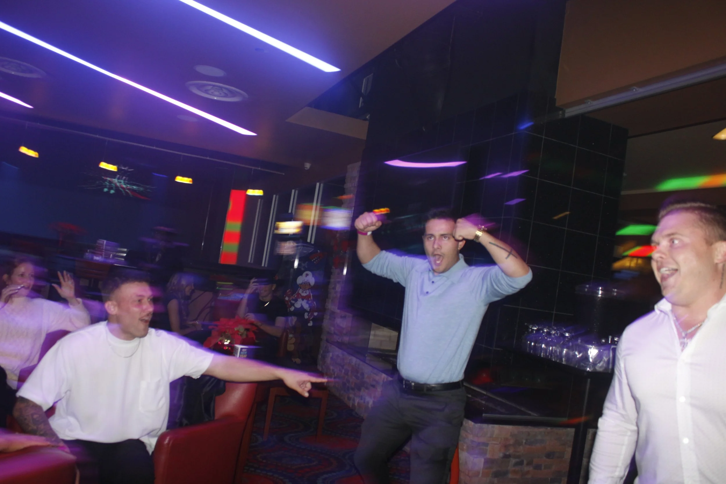 People partying at a nightclub with colorful lights, some individuals dancing and one person flexing muscles, while others watch and have fun.