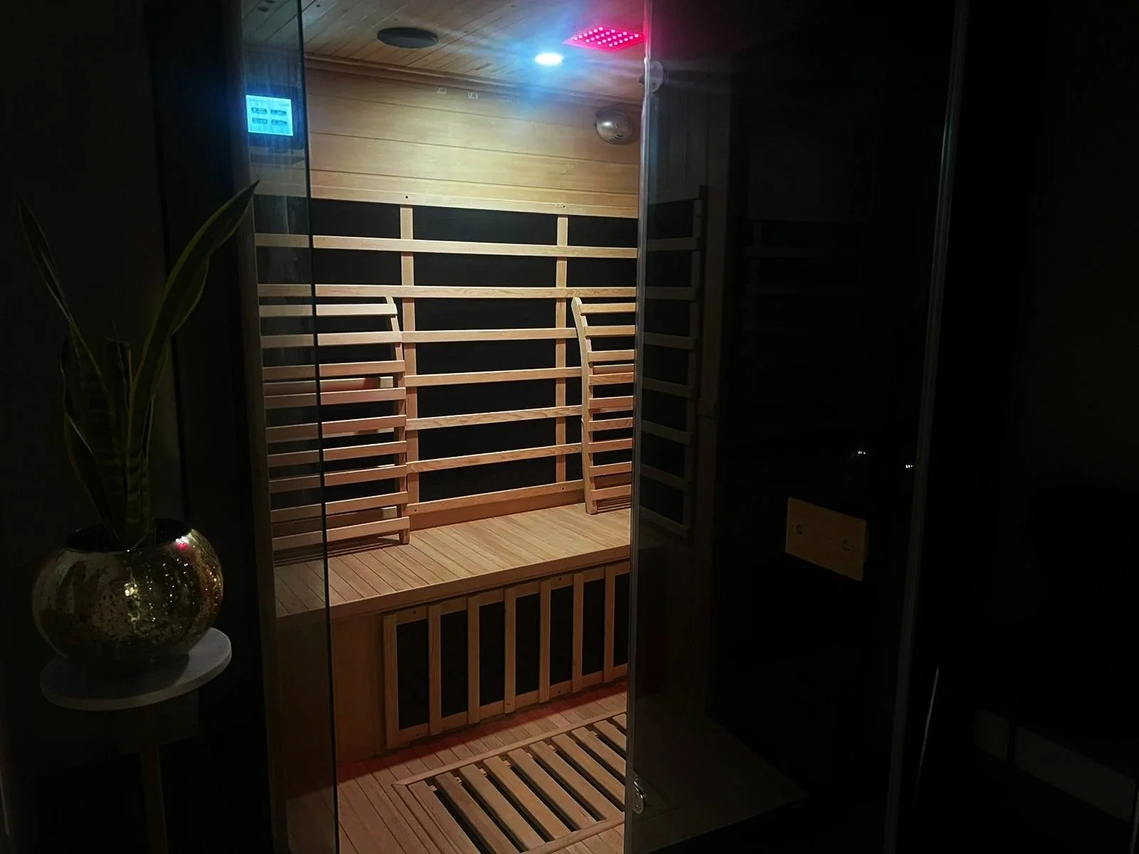Interior of a modern infrared sauna with wooden walls and bench seating, equipped with a digital control panel and ambient lighting.