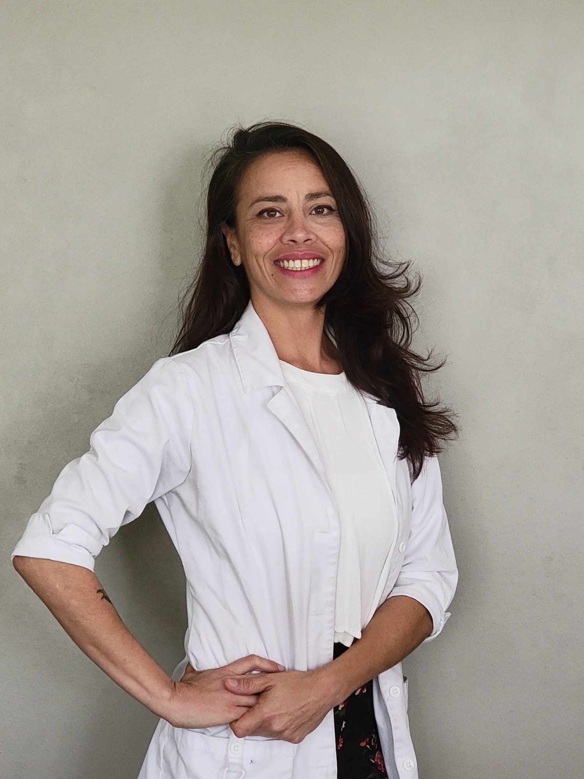 Smiling woman wearing a white coat against a gray background.