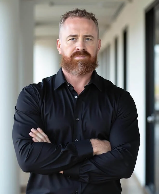 Portrait of attorney Cody M. Brown standing with arms crossed in a black dress shirt.