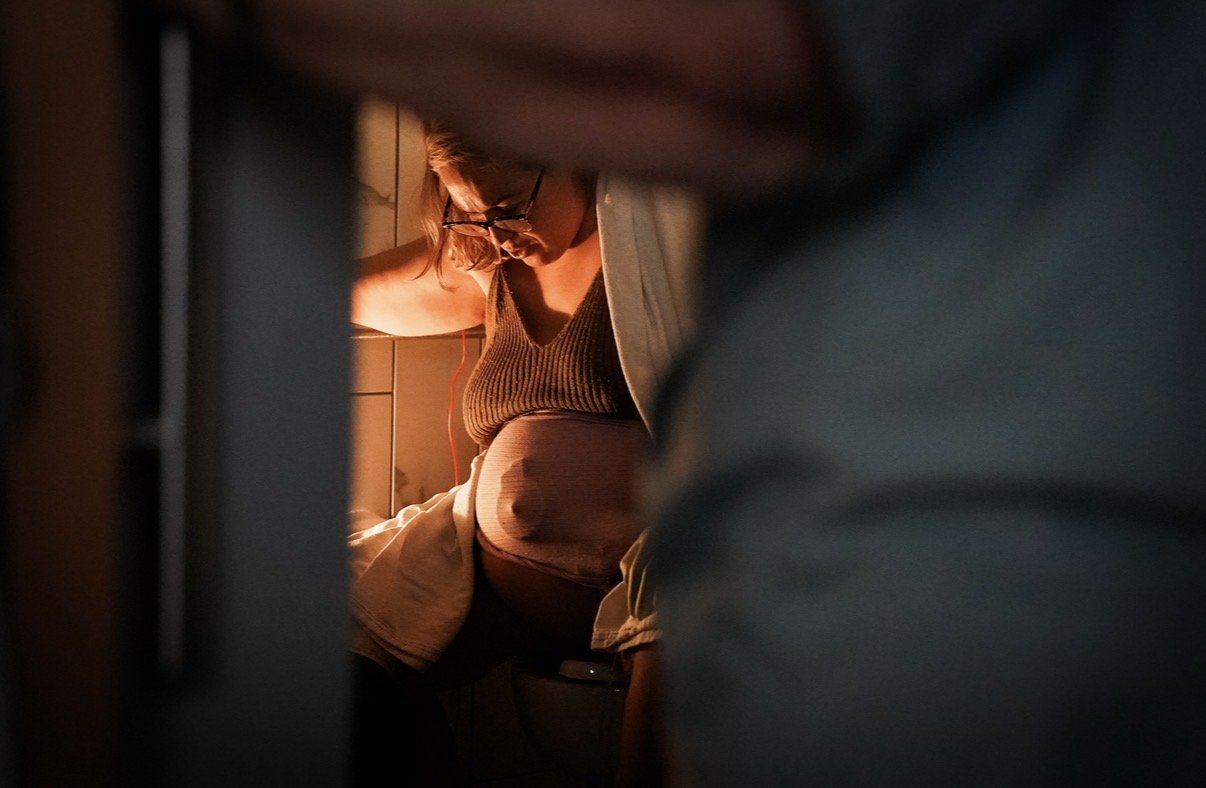 Mother laboring on the toilet in a hospital bathroom at Evanston Hospital near Chicago, with a midwife standing nearby, observing and providing patient support during labor.