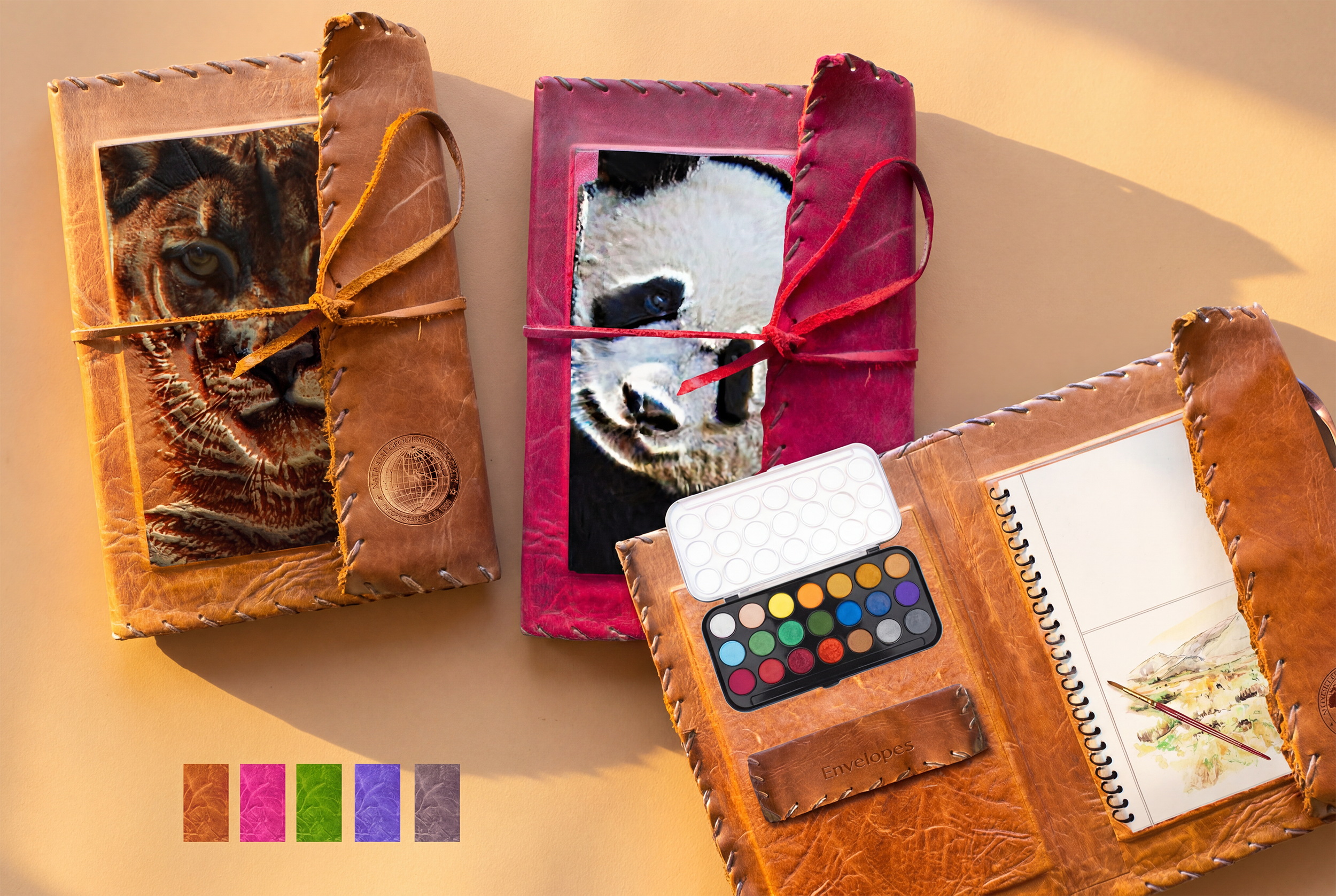 A pair of hand‑stitched leather travel kits featuring deeply embossed and hand‑painted wildlife portraits, produced in collaboration with a Los Angeles leather workshop. One version presents a tiger rendered in warm, natural tones, while the second f