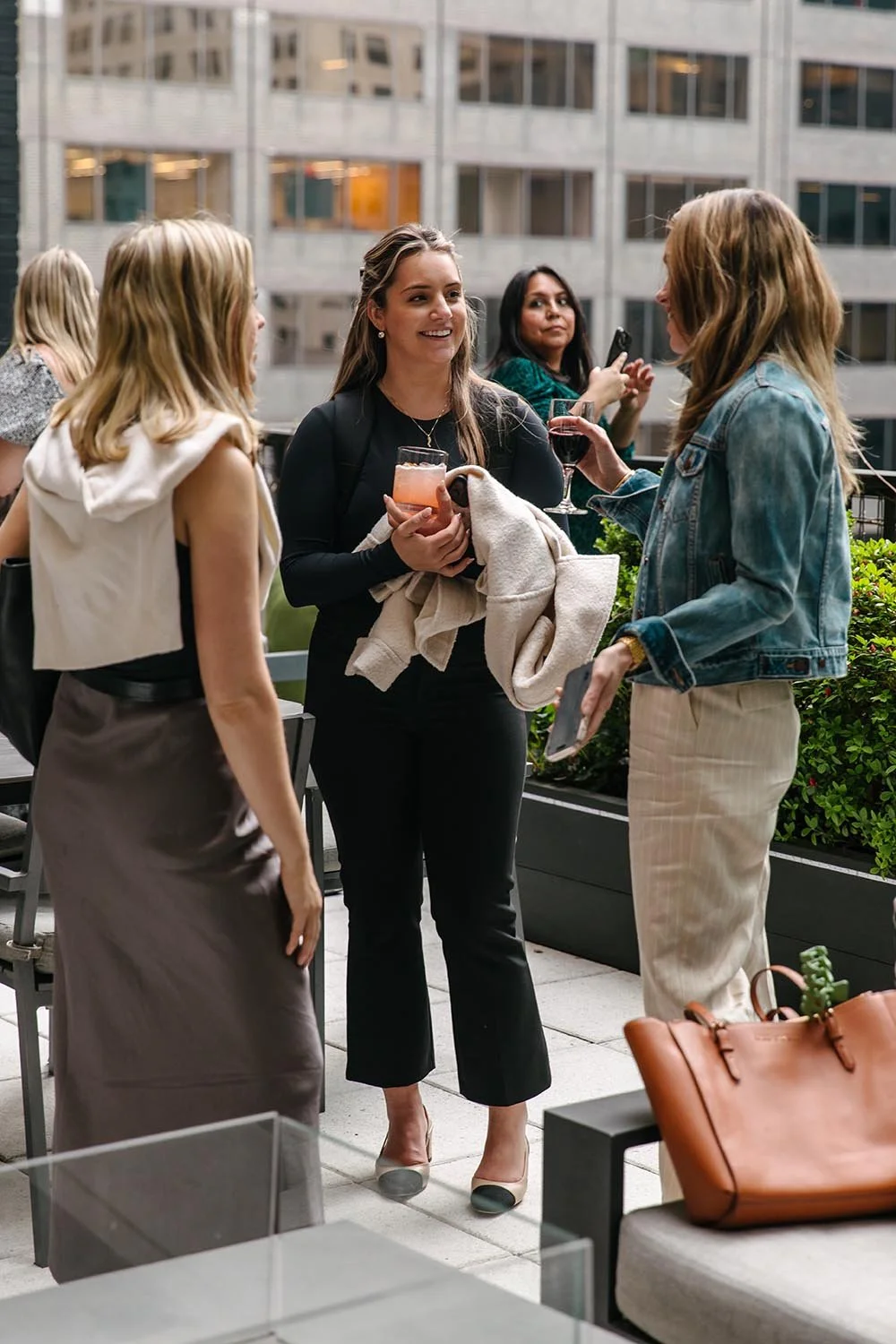 Three women standing outdoors, smiling and talking while holding drinks at a social event