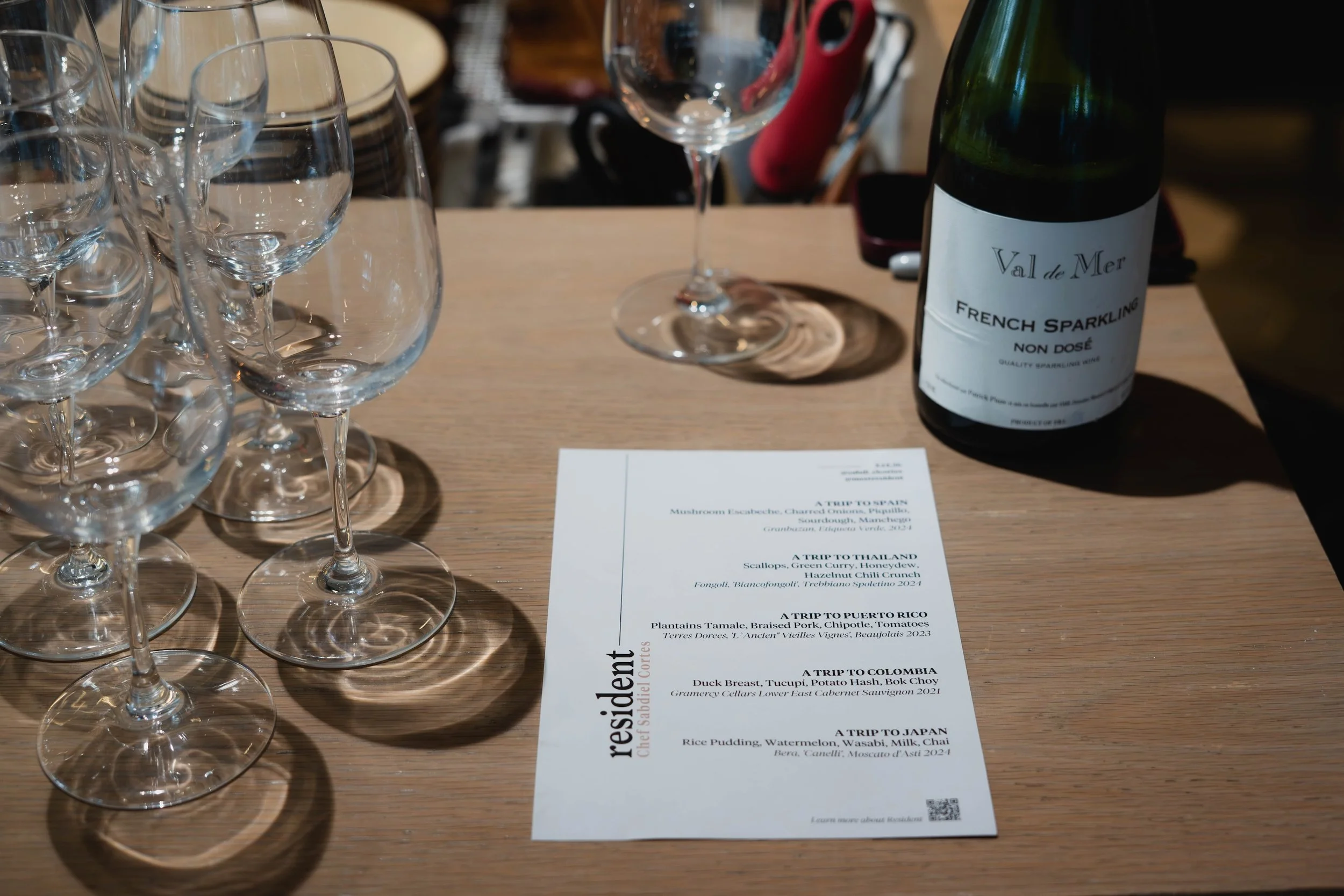 Close-up of a Resident menu laying on a wooden table with a bottle of wine and wine glasses.