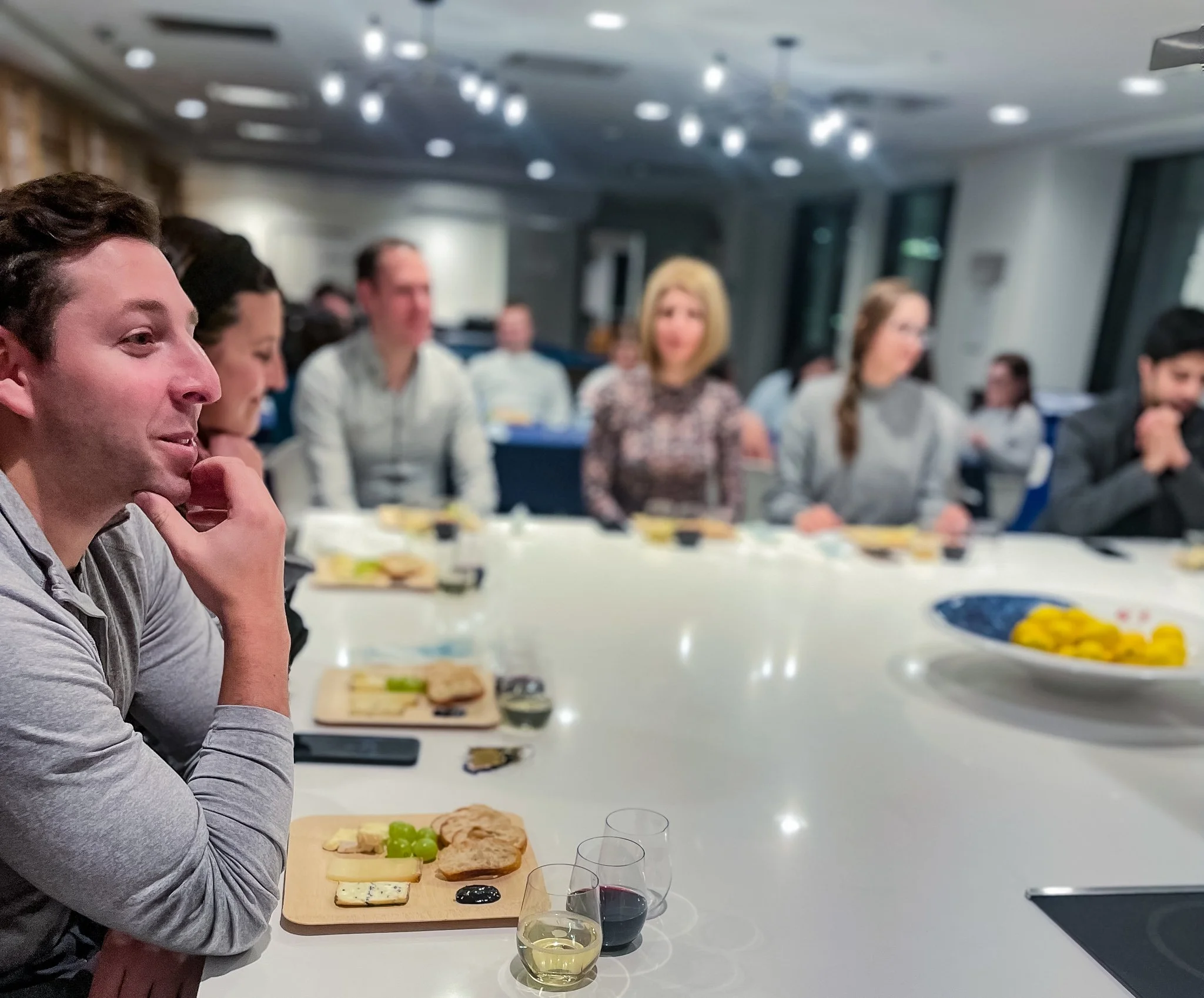 A group of people sitting around a long chef’s counter during a wine and cheese tasting at Resident’s 21 West End venue.