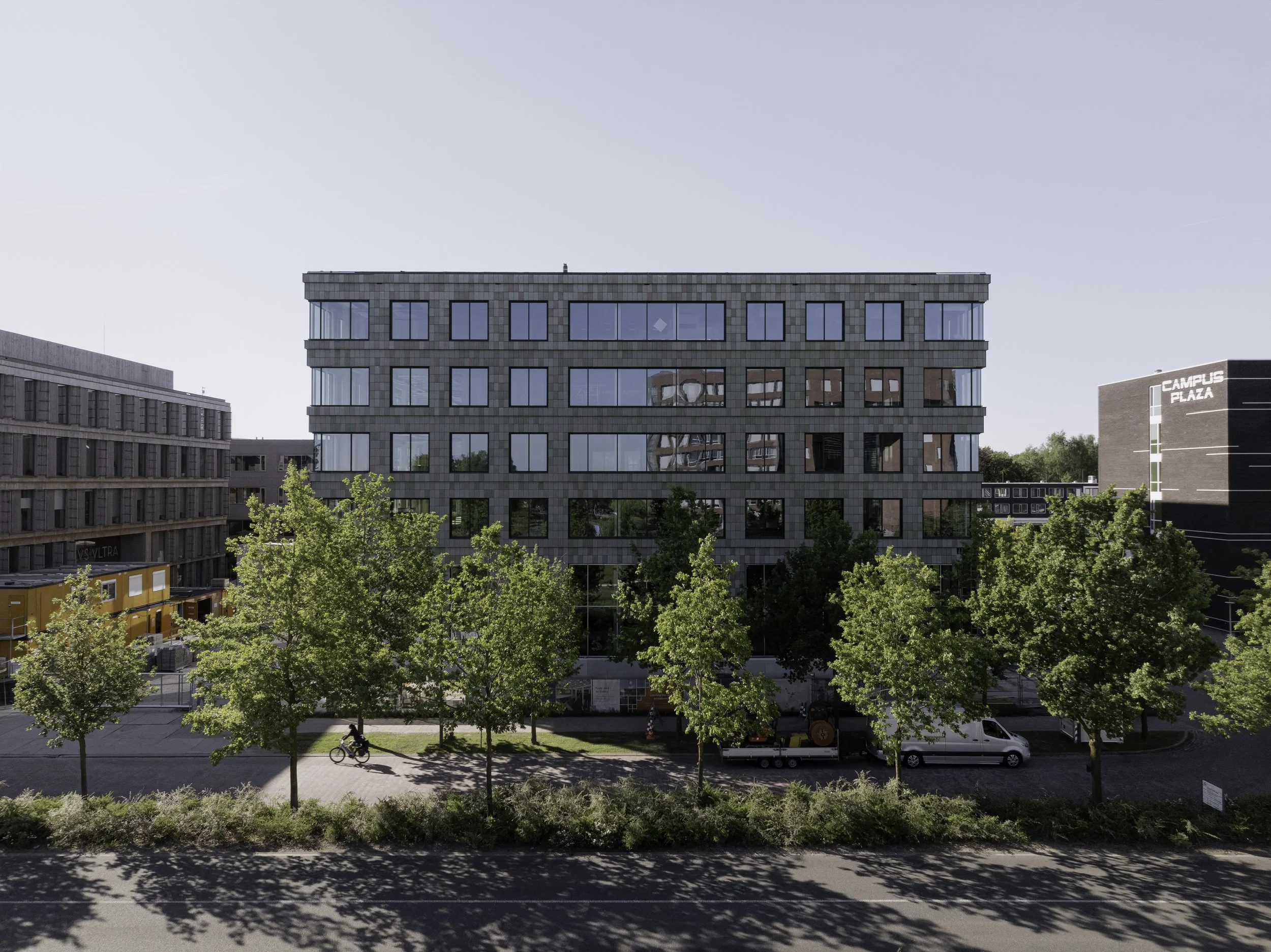 Atmospheric context shot of Plus Ultra III surrounded by other sustainable buildings on campus. The light reflections on the façade surface highlight the texture and materiality of the recycled cladding.