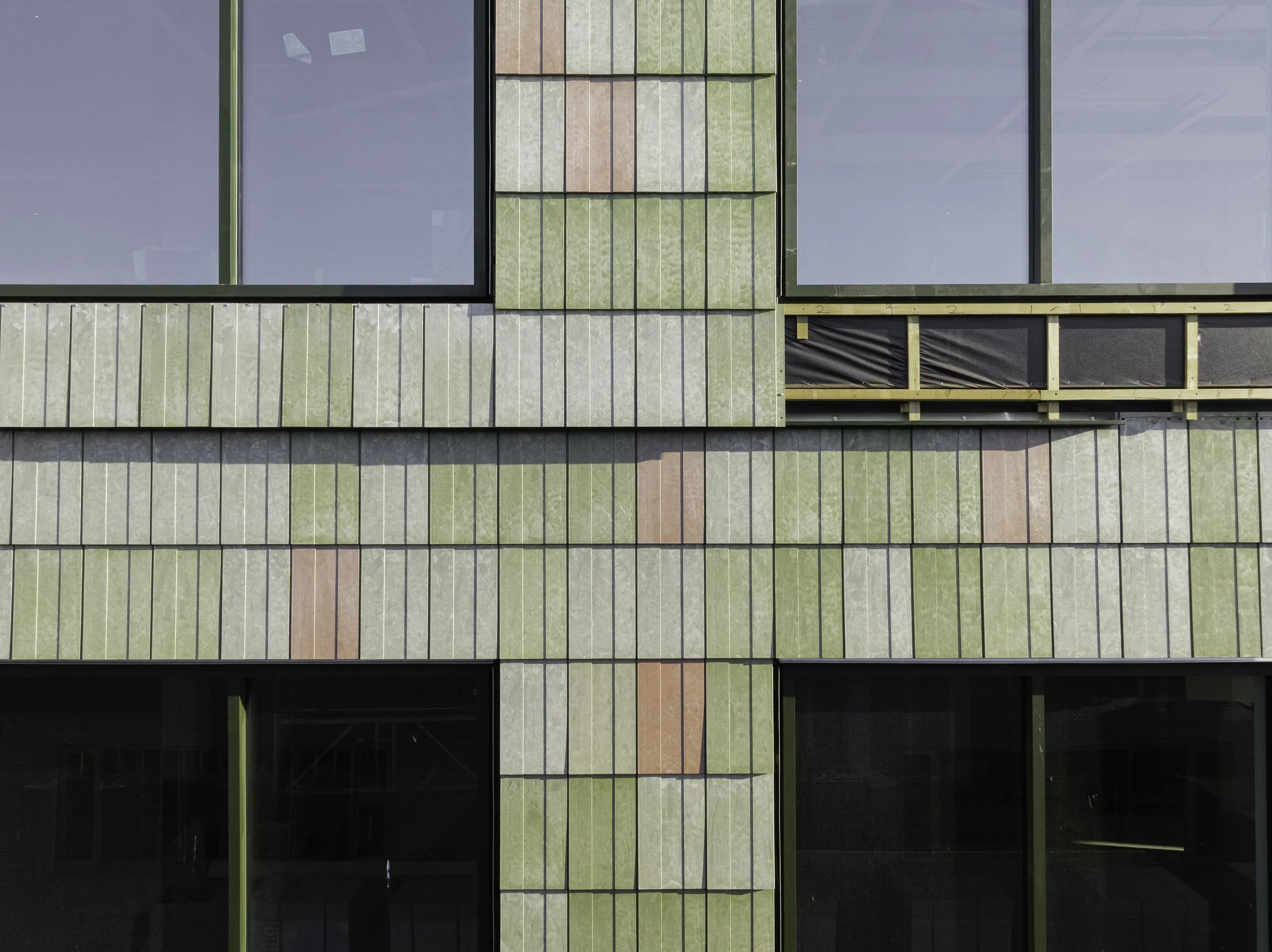 Close-up of the circular façade at Plus Ultra III, clad with Basic Third tiles made from 100% recycled PVC. The vertical lines and subtle colour variations in green and terracotta highlight the aesthetic potential of sustainable materials.