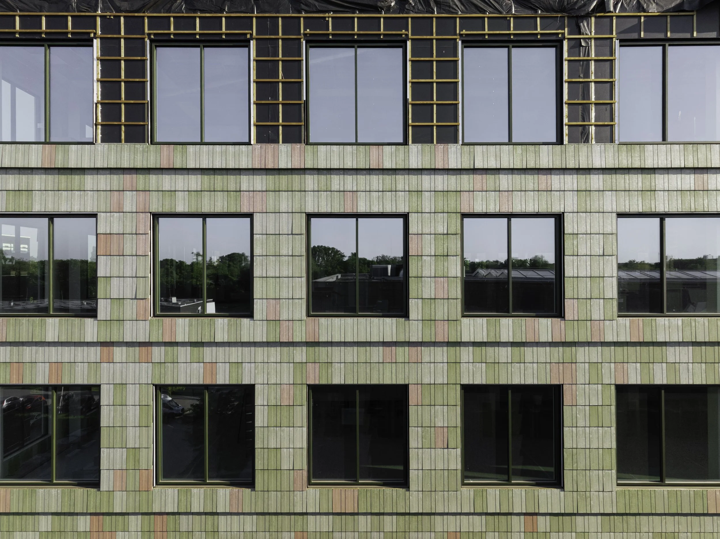 Vertical composition of the building under construction, showing both the recycled façade panels and the underlying grid for insulation and fixings. A strong visual link between architectural design and technical execution.