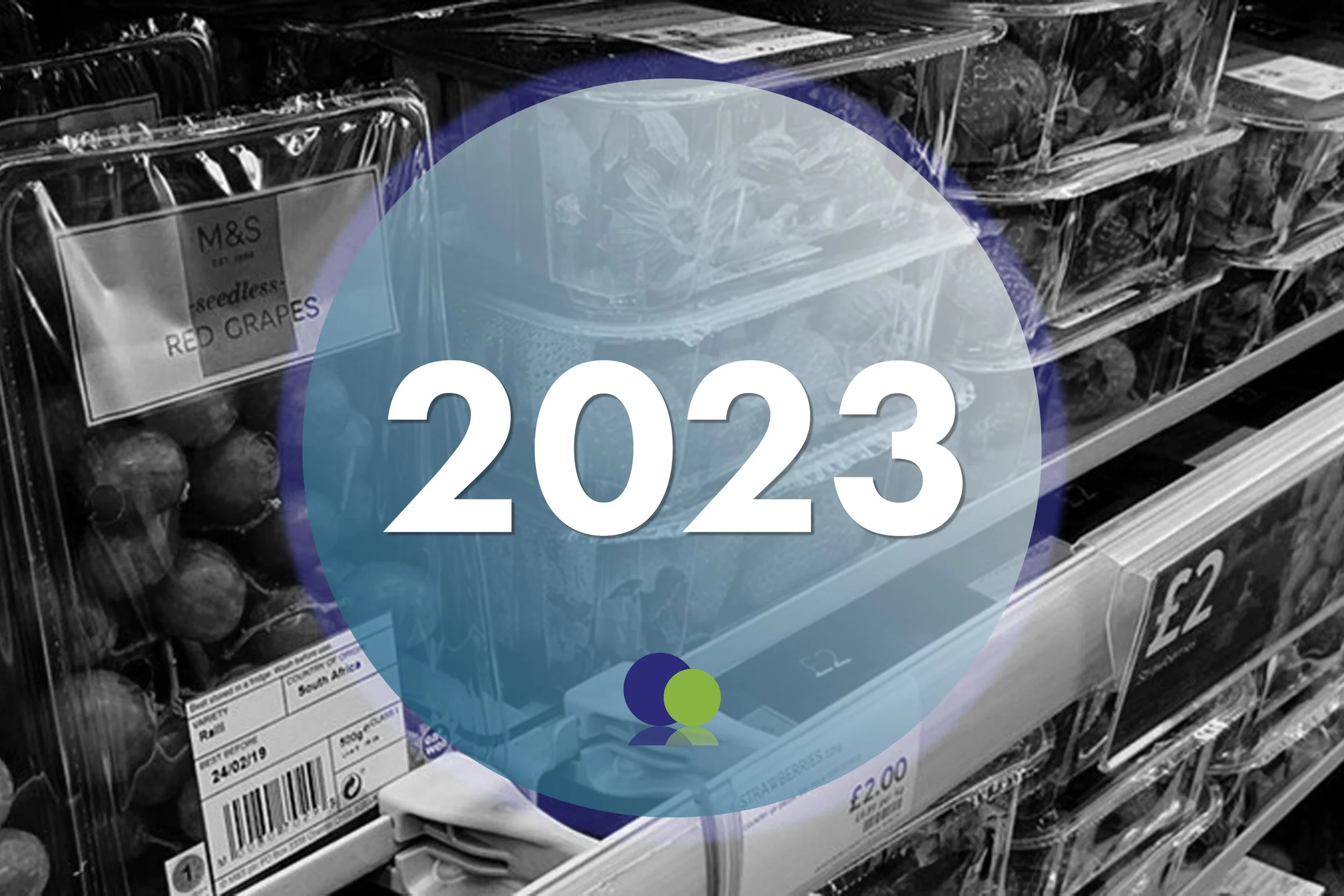Étagère de baies mélangées, y compris des raisins, dans une épicerie, avec un grand cercle bleu affichant "2023" en texte blanc.