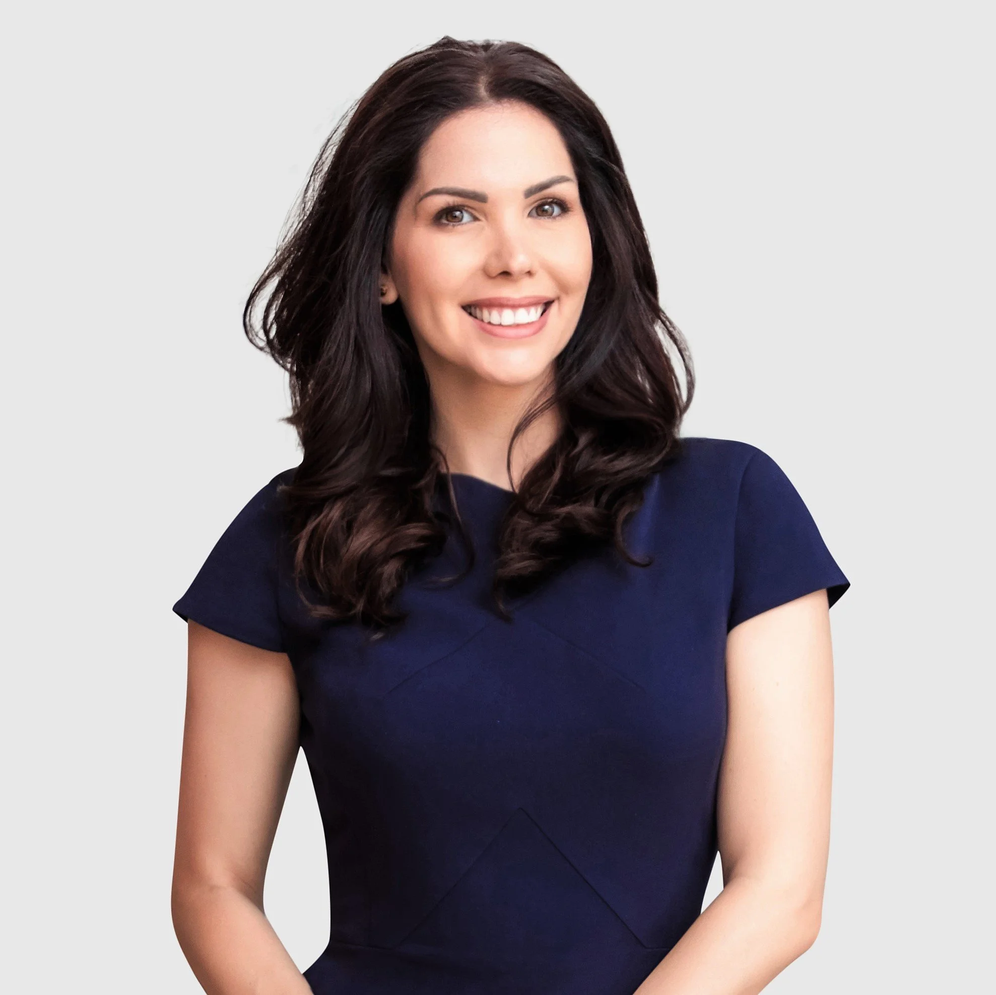 A woman with dark brown wavy hair smiling and wearing a navy blue dress against a plain light background.