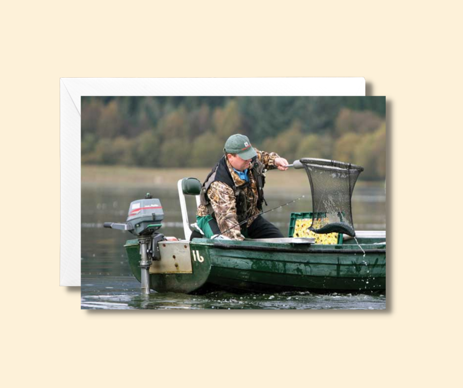 Anglers greeting card of a fly fisherman in a small boat on a lake landing his catch in a net. Size 20 x 14 cm
