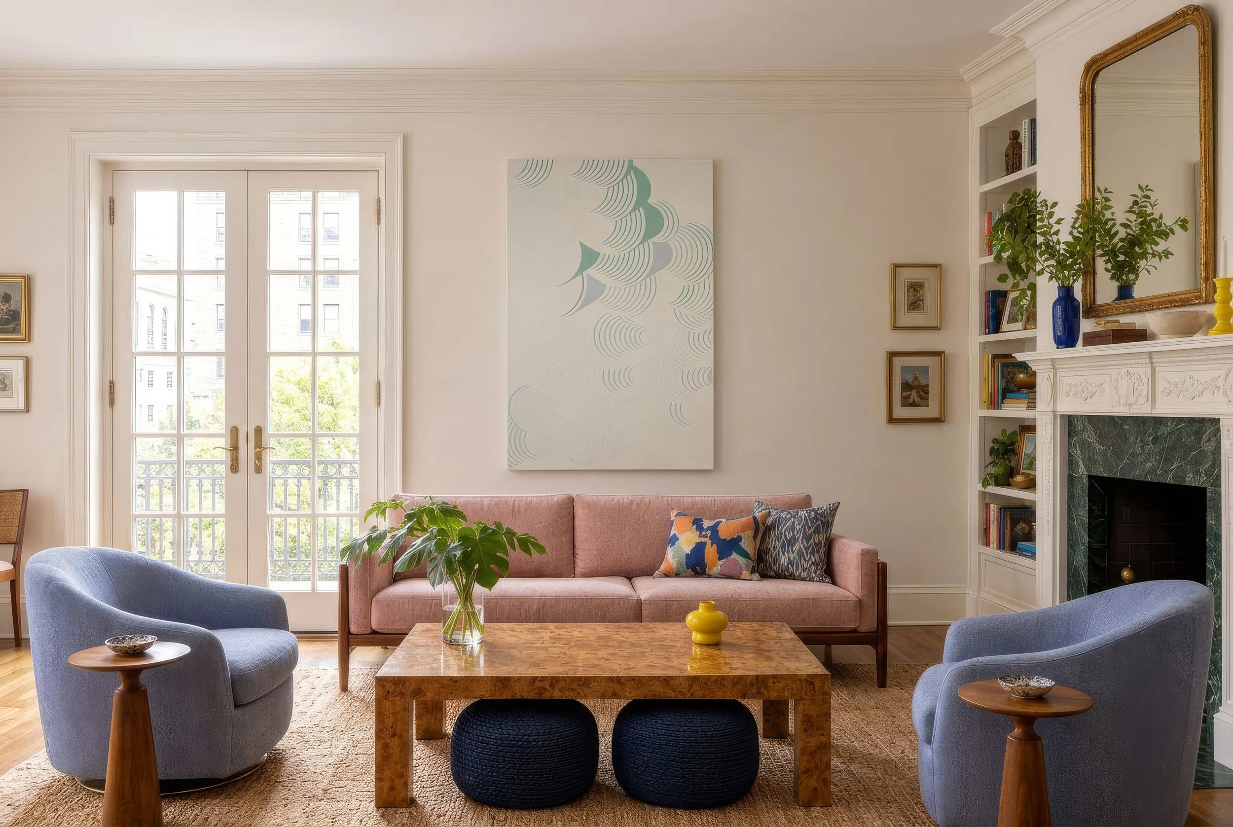 A sunlit living room with a large white artwork of mint and gray arches hanging above a pink sofa.
