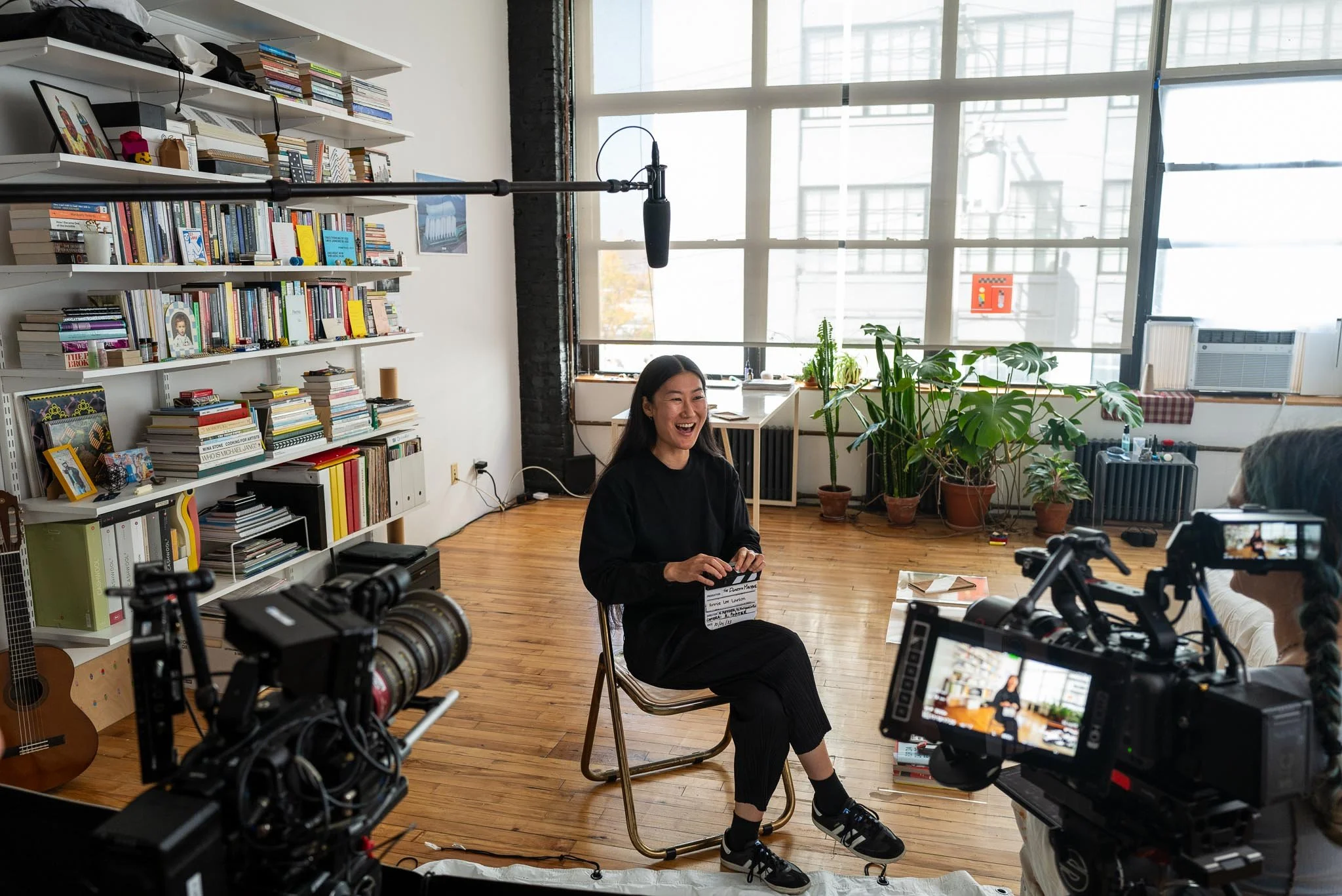 Annie Lee Larson holds the slate before her interview, in the middle of her Brooklyn loft surrounded by books and plants.