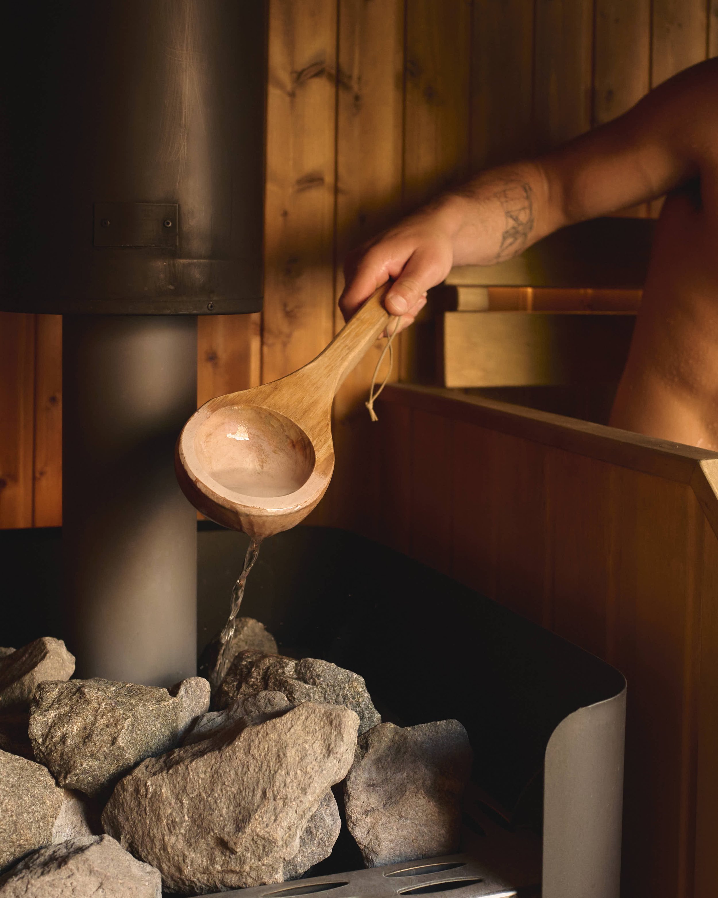 Customer using ladle to apply water over hot stones inside Saela Sauna Ouseburn for commercial content and business brand photography in Newcastle 