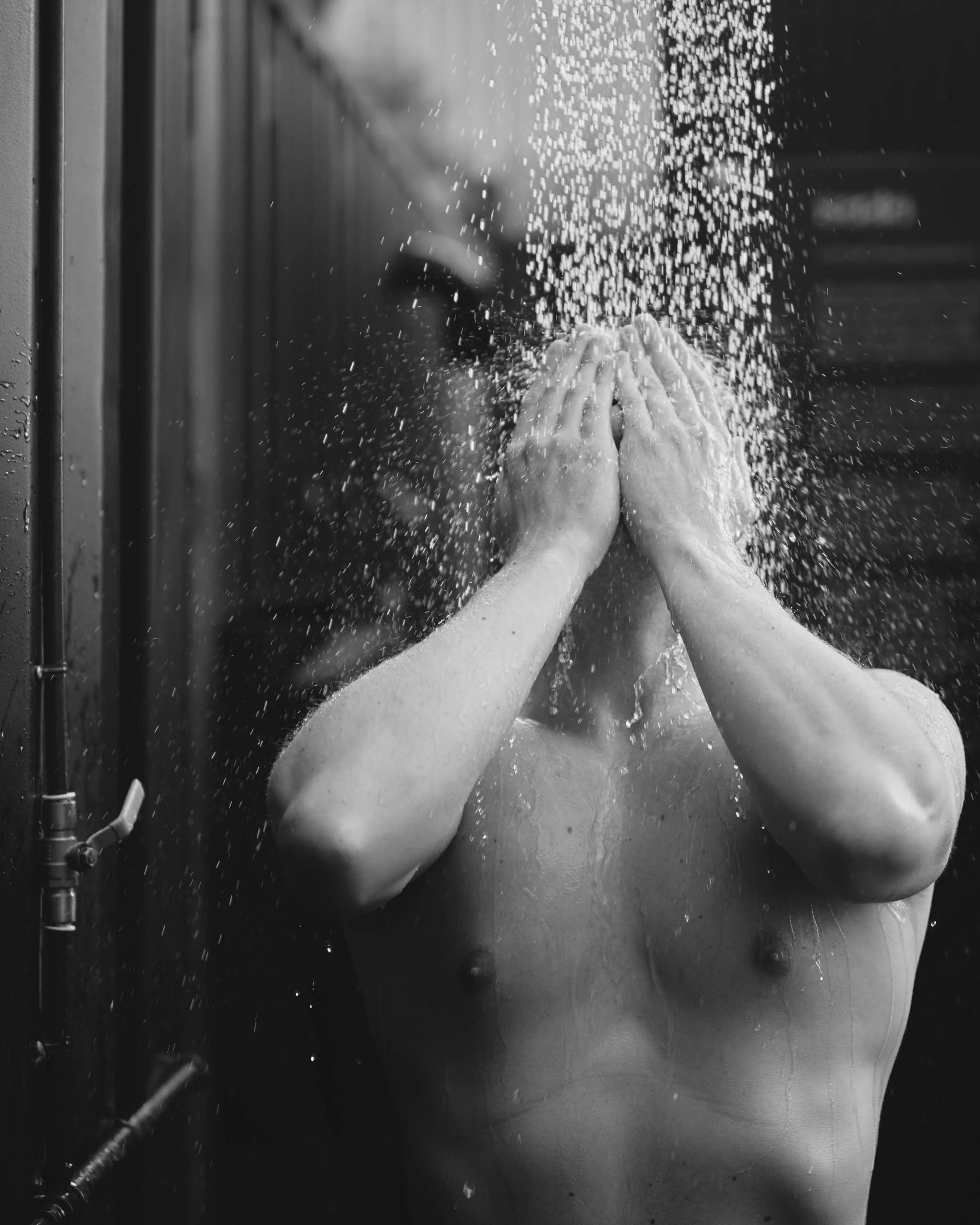 Black and White image of male Saela Sauna customer slashing face in a cold shower post sauna before getting into the cold plunge for commercial artistic brand photography in Newcastle Upon Tyne North East UK