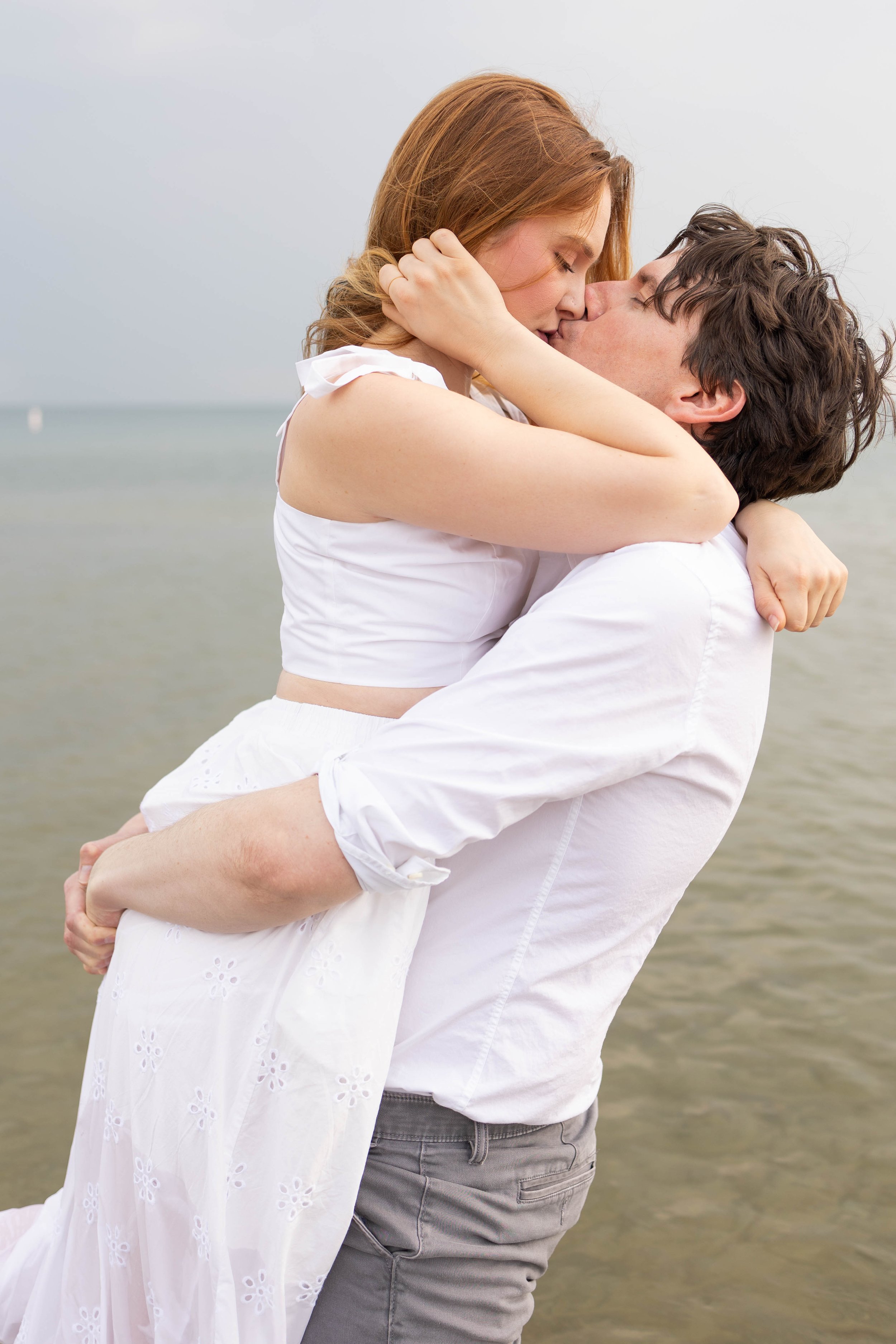 A couple sharing a kiss at the beach, with the man lifting the woman in his arms.