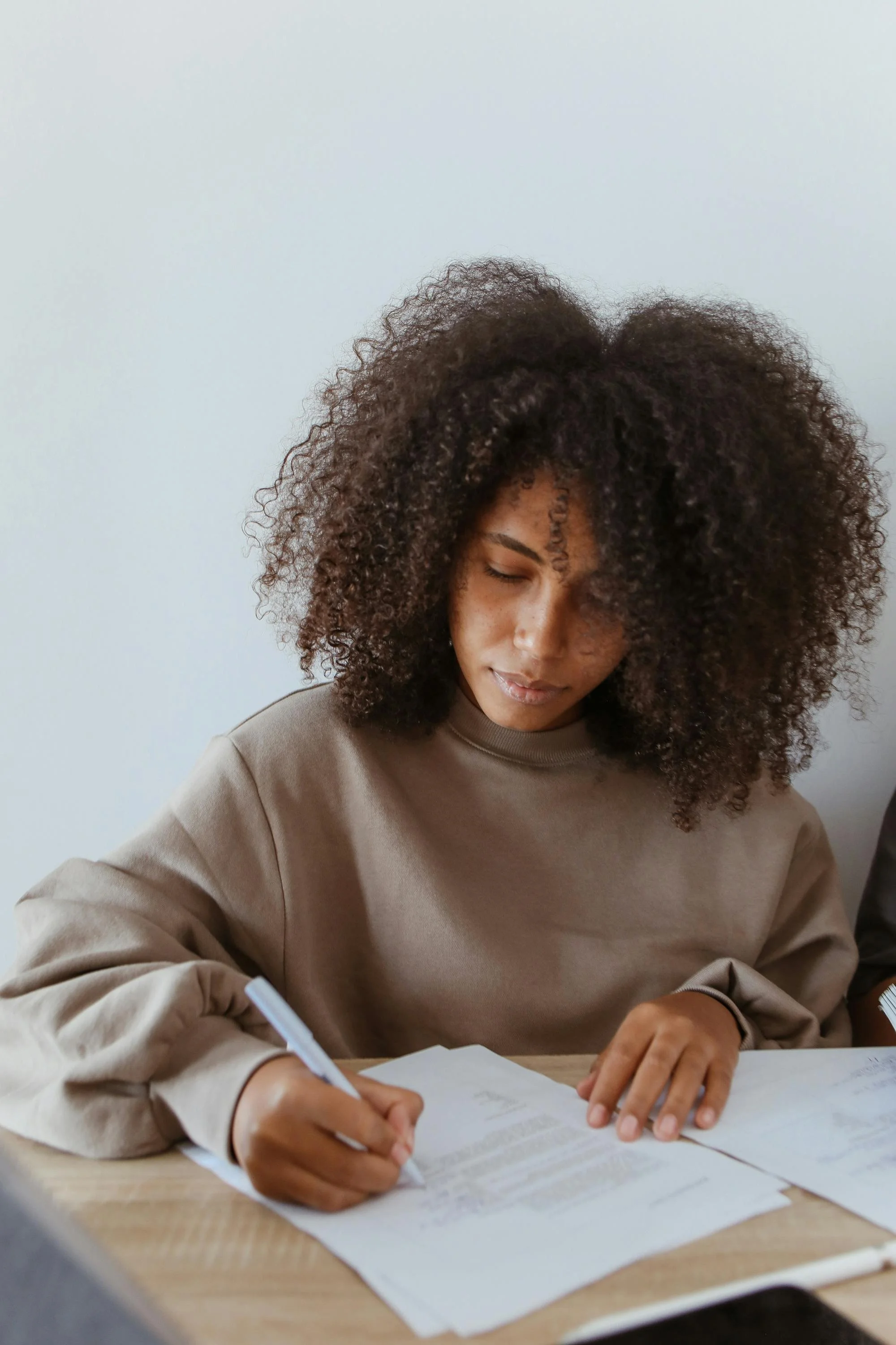 A young woman with curly hair writing on papers at a desk