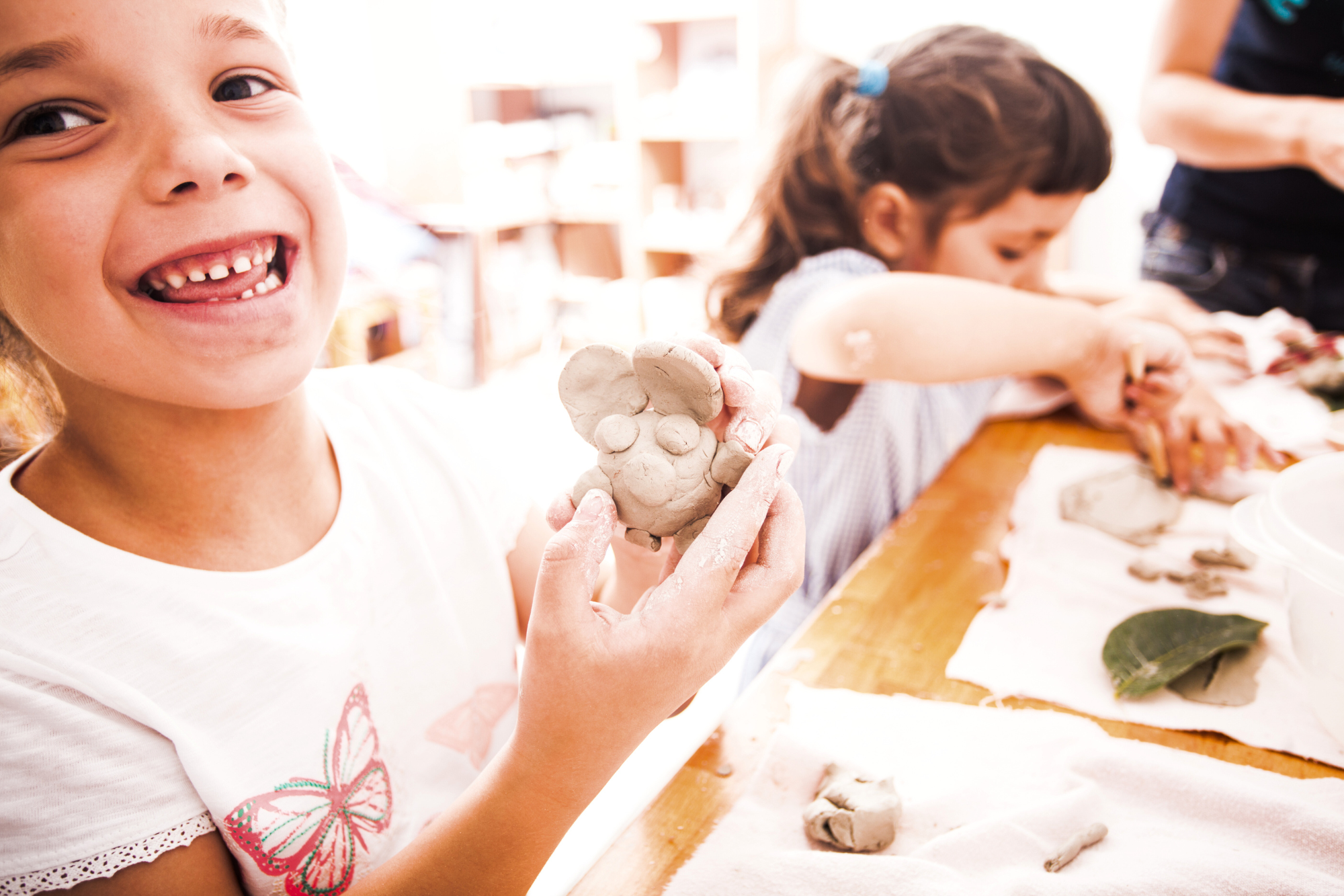 a child smiling as they hold up their model clay figure