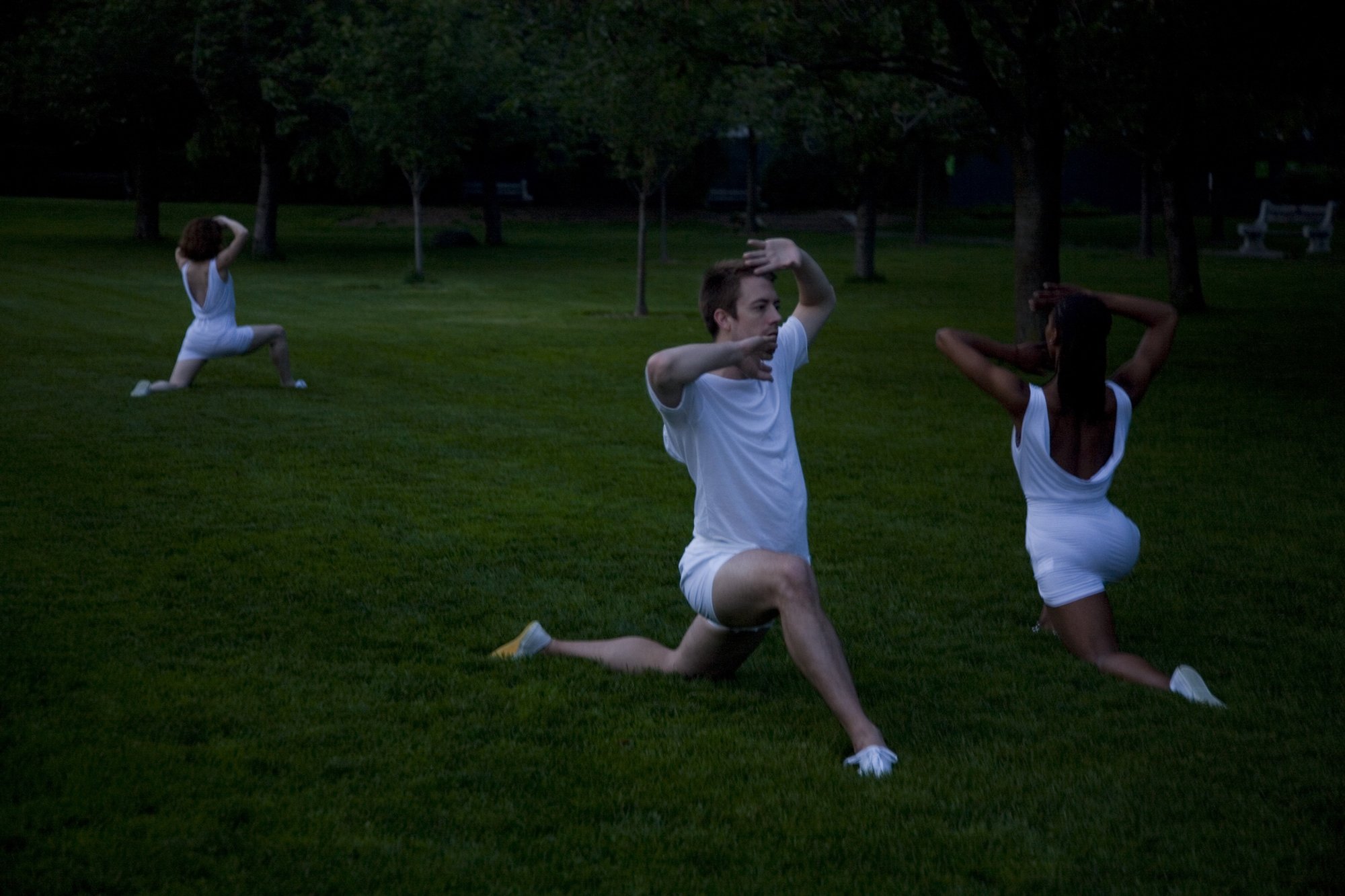 Performers in white kneeling in a green field. Photo by Kevin Kwan.