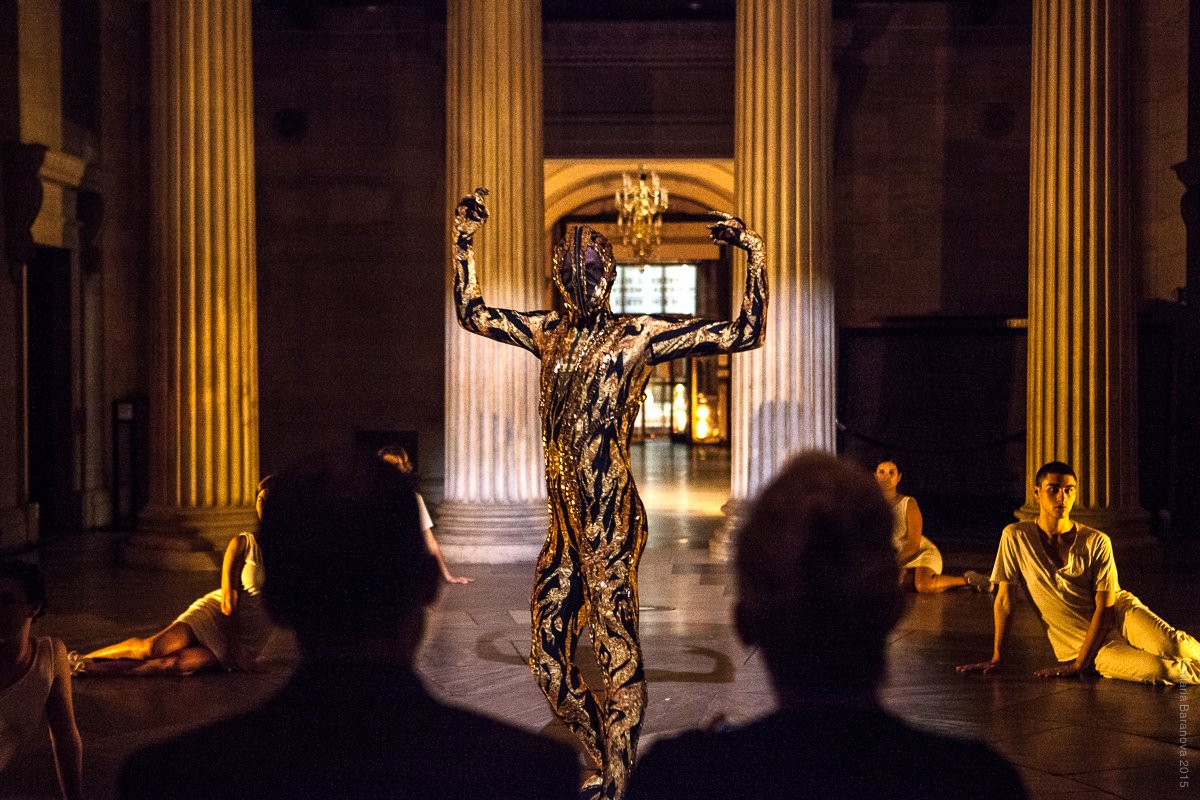 A performer stands with his arms raised wearing a gold sequin bodysuit at the Rotunda at Federal Hall. Photo by Maria Baranova.