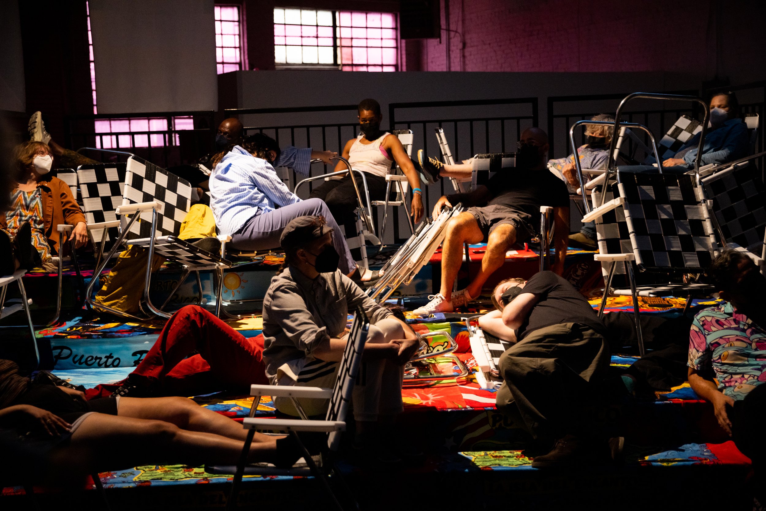 An audience lounges on a platform covered with Puerto Rican beach towels and strewn with black and white lawn chairs. Photo by Maria Baranova.