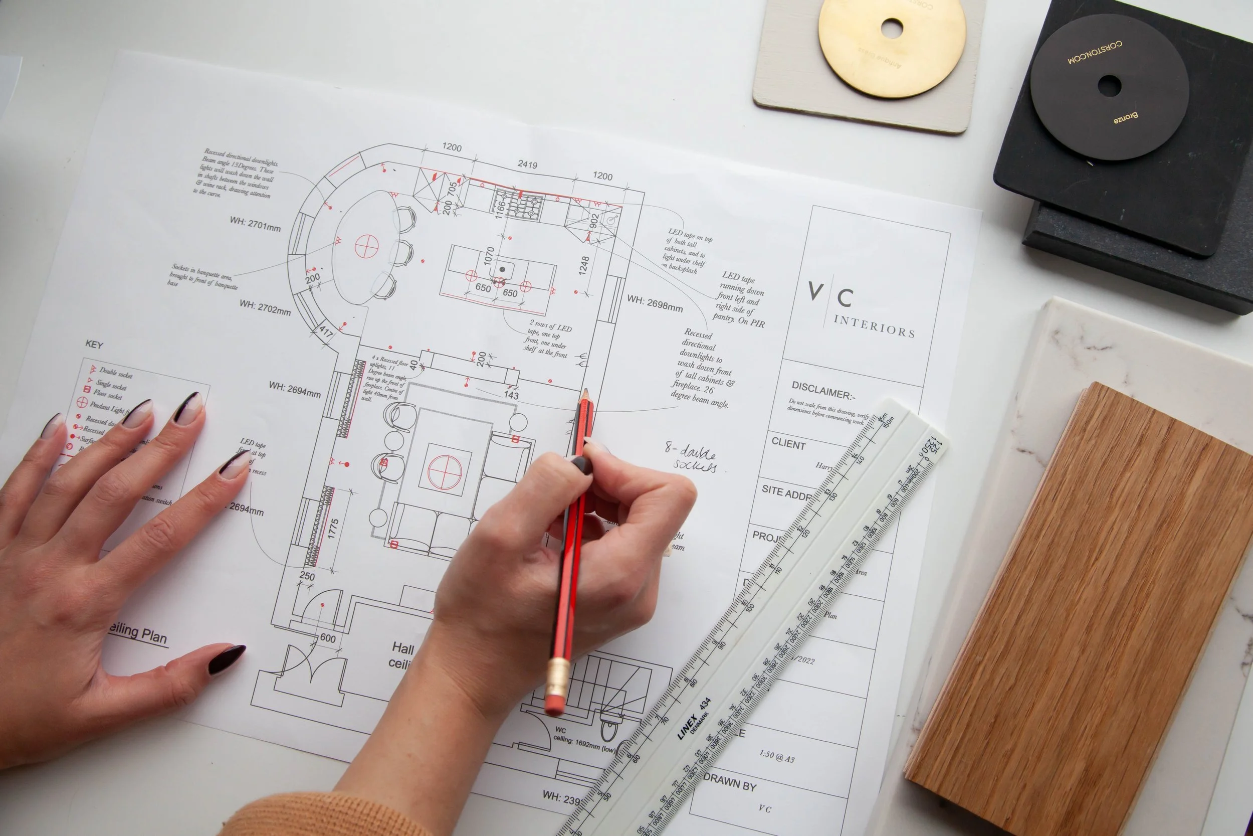 Architect working on interior design blueprints with a ruler and color sample swatches on a white desk.