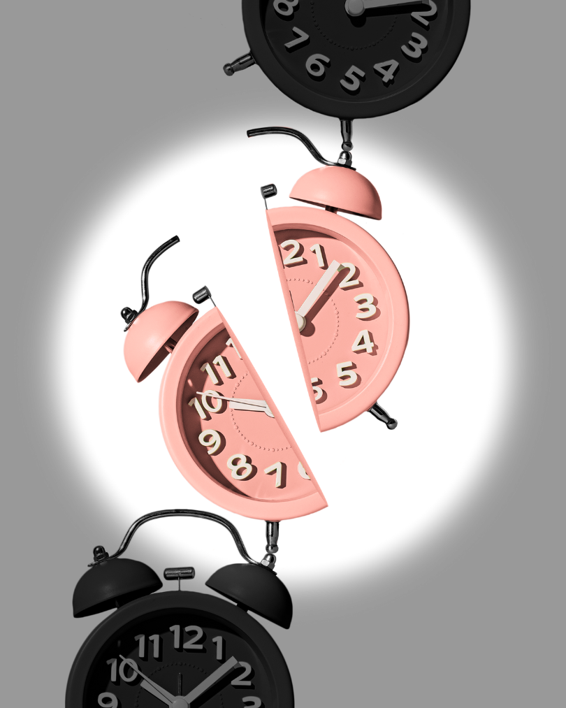 An image by Shamblen Studios of vintage alarm clocks stacked upon each other. The clock in the middle is broken in half.