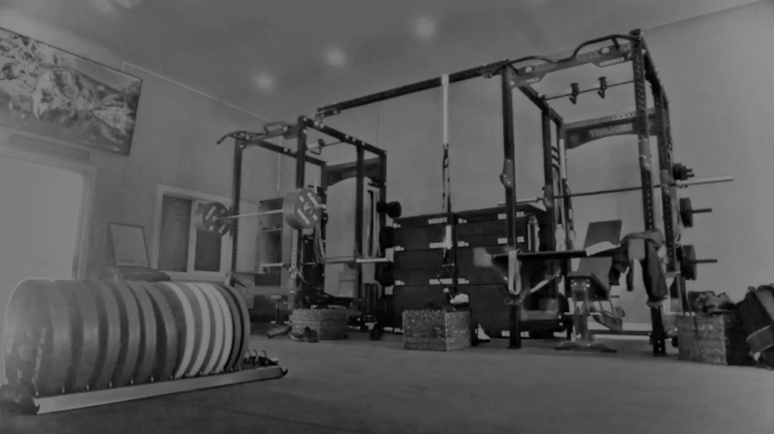 Home gym setup with a power rack, barbells, weight plates, a medicine ball, foam rollers, and a television on the wall.