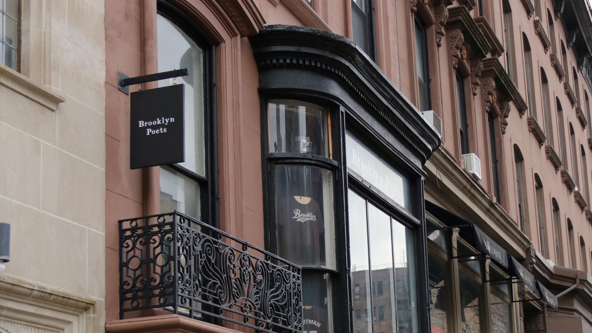 Historic brownstone building with ornate iron railing and a "Brooklyn Poets" sign