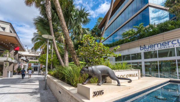 Outdoor shopping area with a panther sculpture, green plants, and modern glass buildings, including a Bluemercury store.