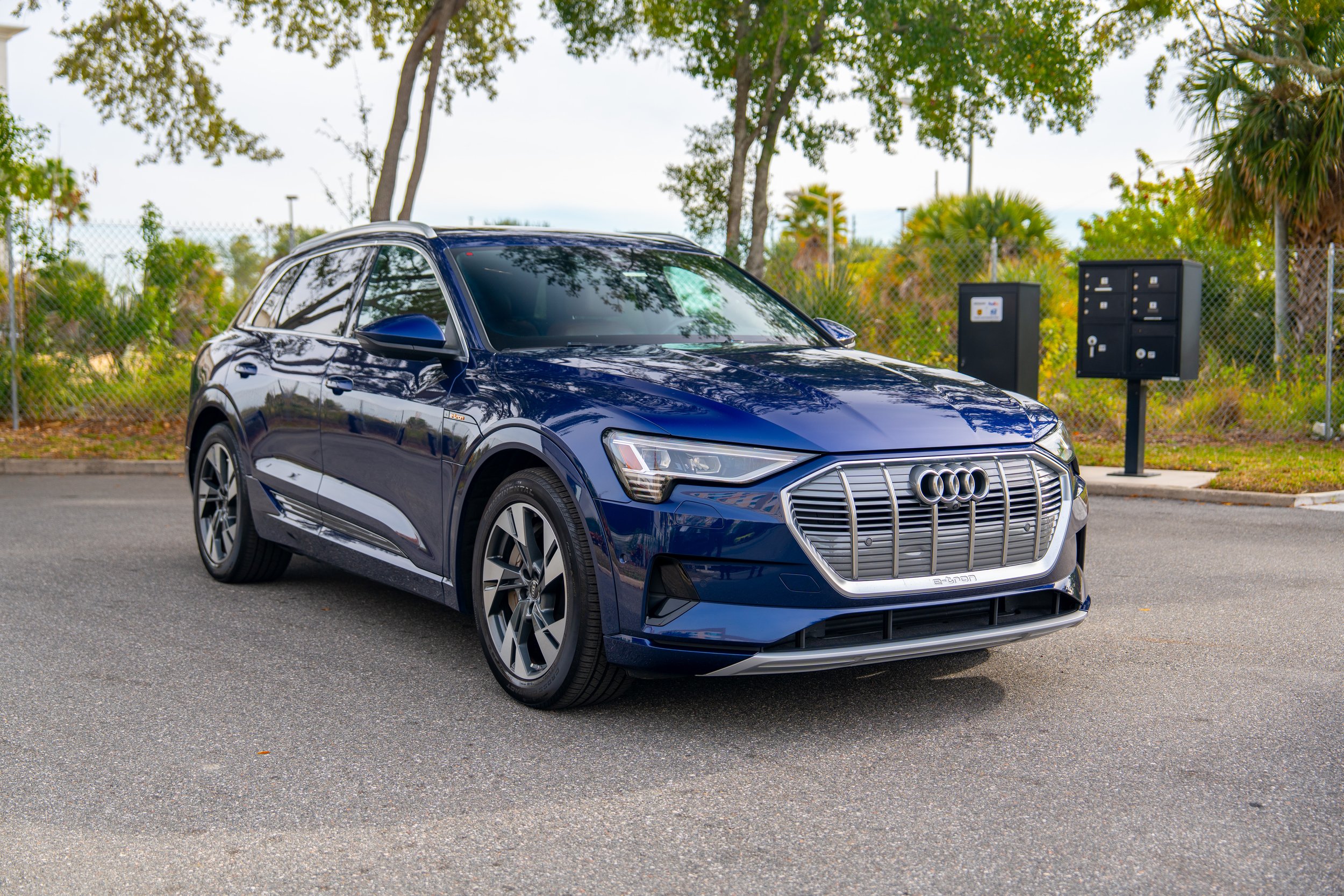 A dark blue Audi SUV parked on an asphalt road with trees and mailbox in the background.
