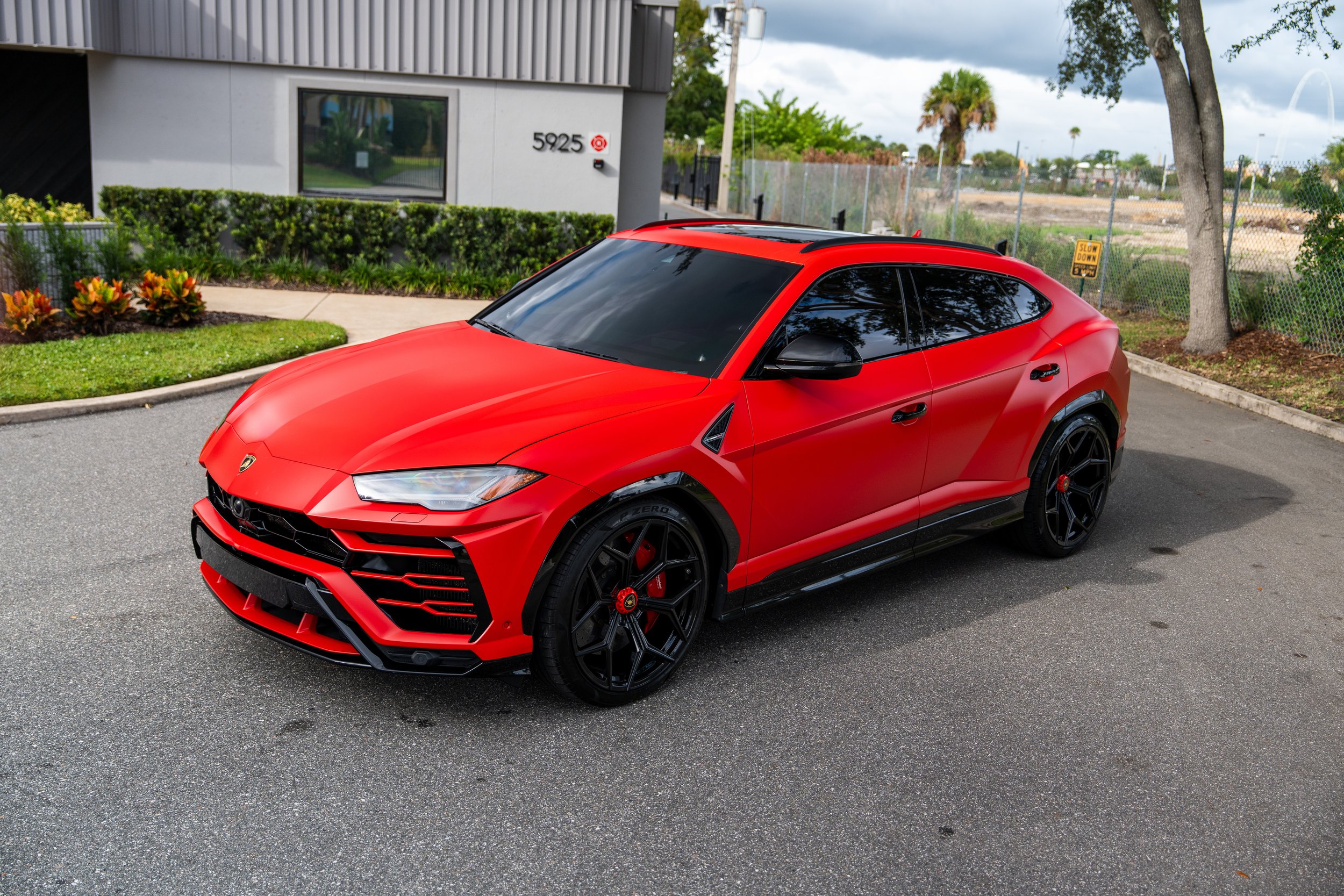 Red sports car, Lamborghini, parked on a street with trees and buildings in the background.