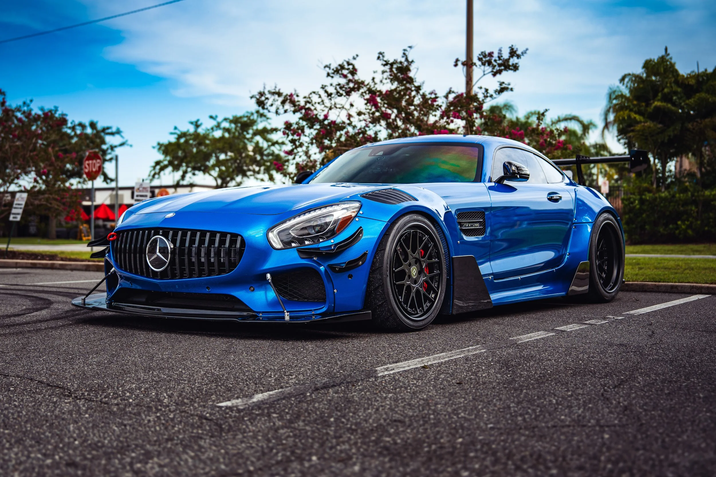 Blue Mercedes-Benz race car parked on the street with trees and stop sign in the background.