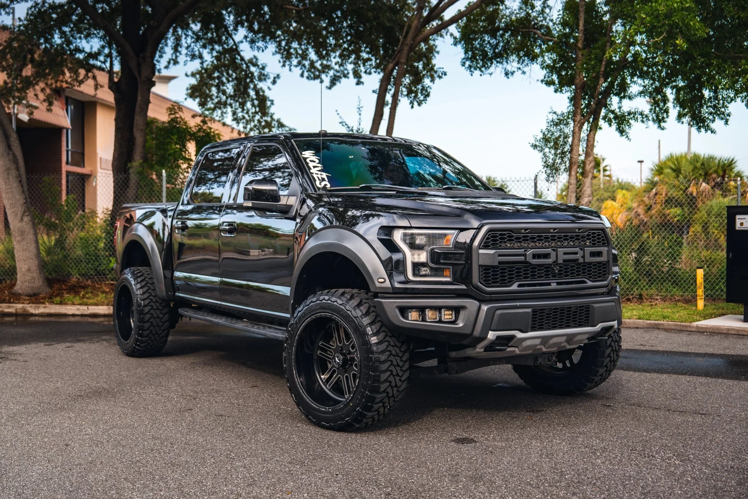 Black Ford pickup truck with large tires parked outdoors near trees and a building.