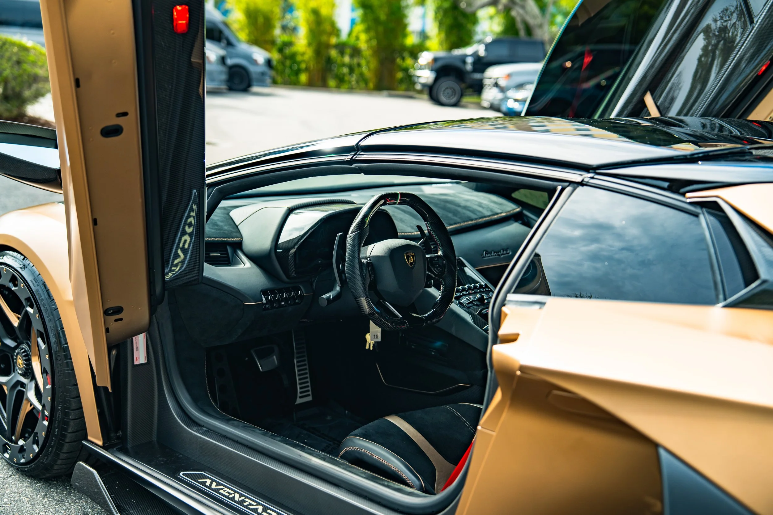 Interior of a Lamborghini supercar, showing the steering wheel, dashboard, and seats, with a gold exterior paint.