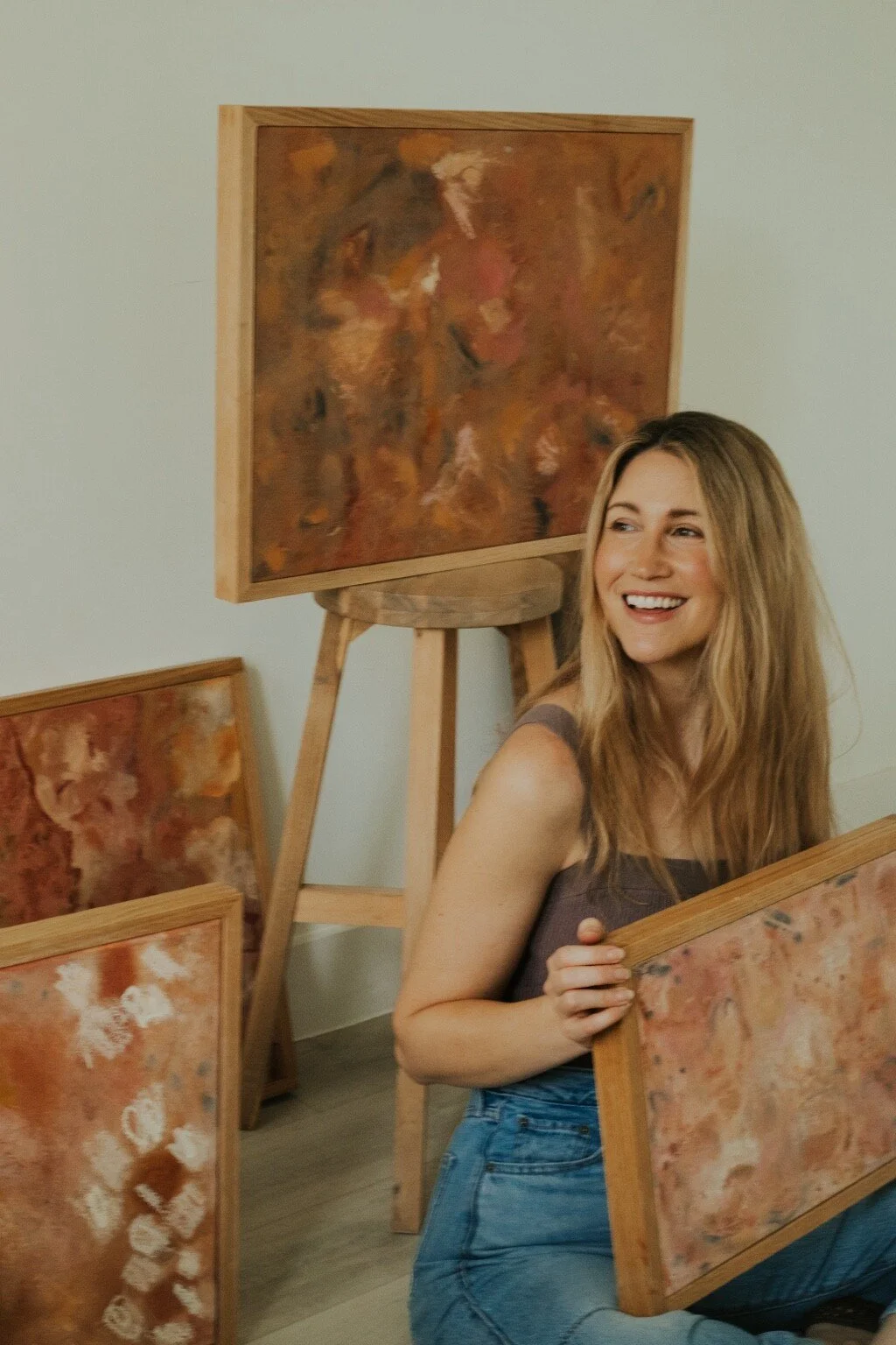 Whitney smiling while seated among her original abstract paintings