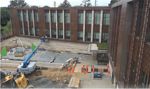 Construction site in front of a multi-story building, with equipment, orange traffic cones, and workers
