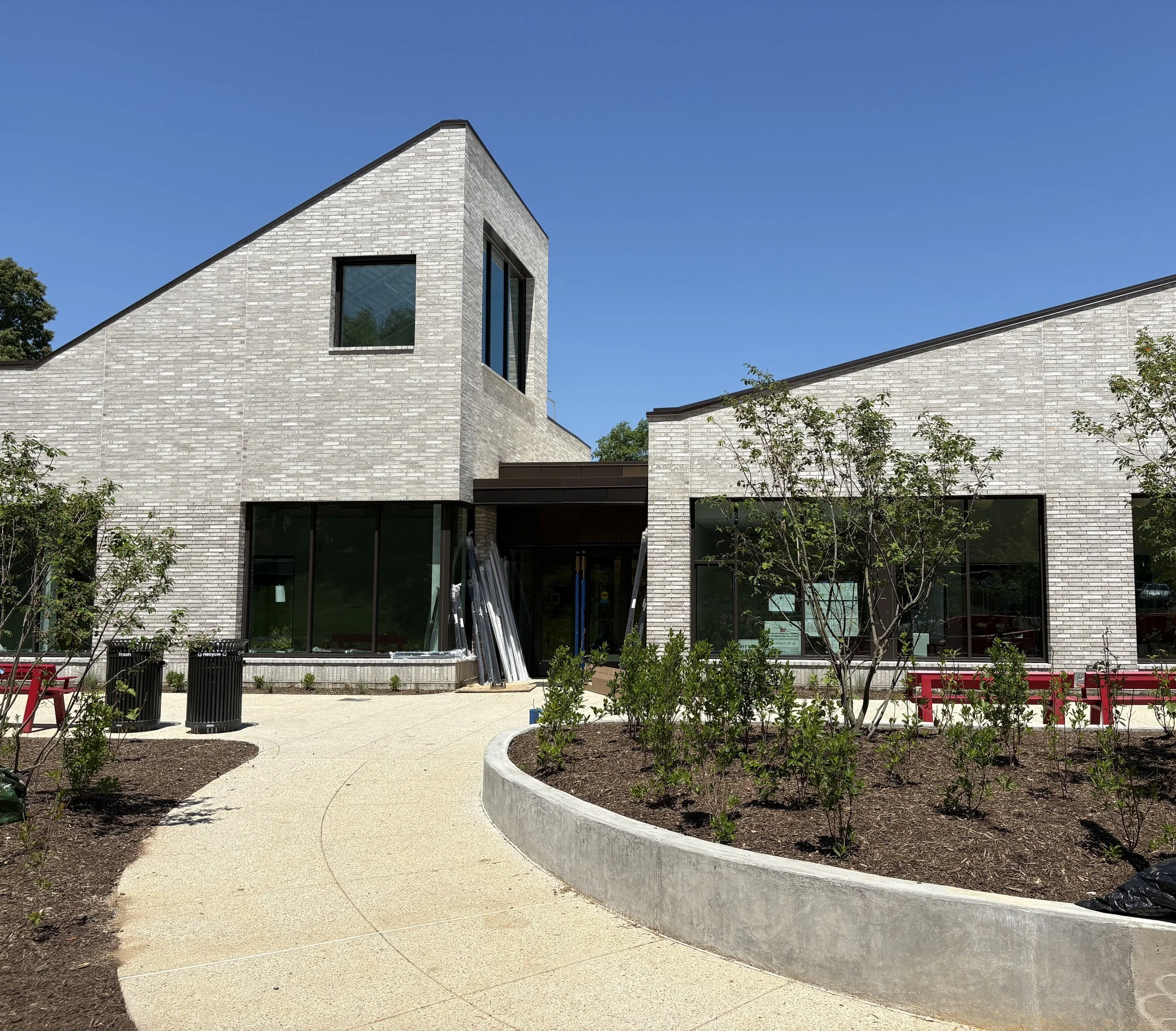 Modern white brick building with large windows under a clear blue sky, with landscaped garden and benches in the foreground.