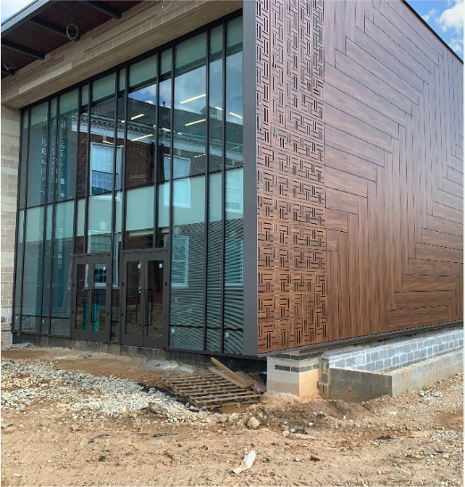 Exterior of a modern building with glass windows and a wooden wall with decorative patterns.