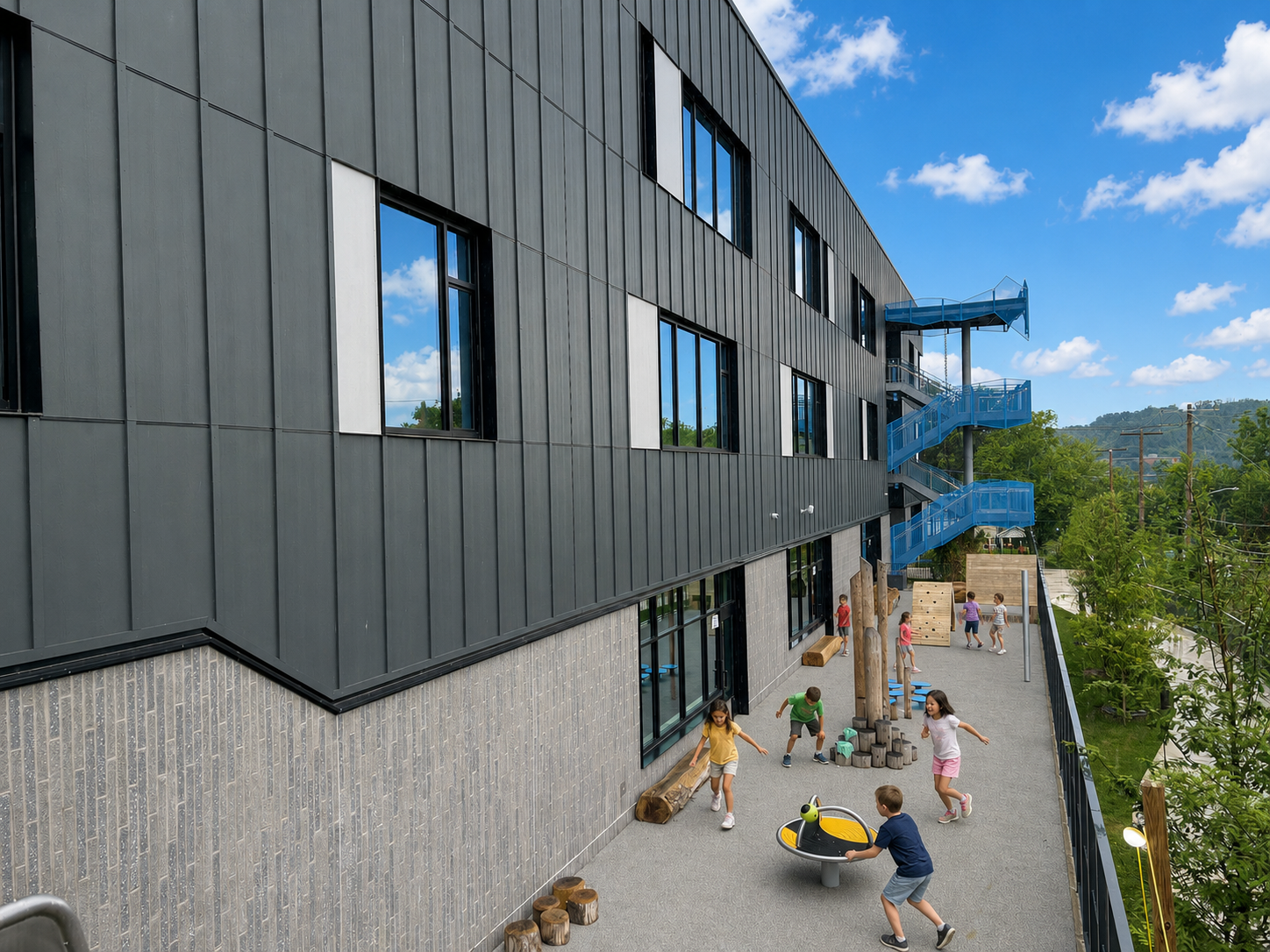 Children playing outside on a concrete area near a modern building with black metal siding and large windows, featuring a blue spiral staircase attached to the exterior. The background shows trees and a blue sky with clouds.