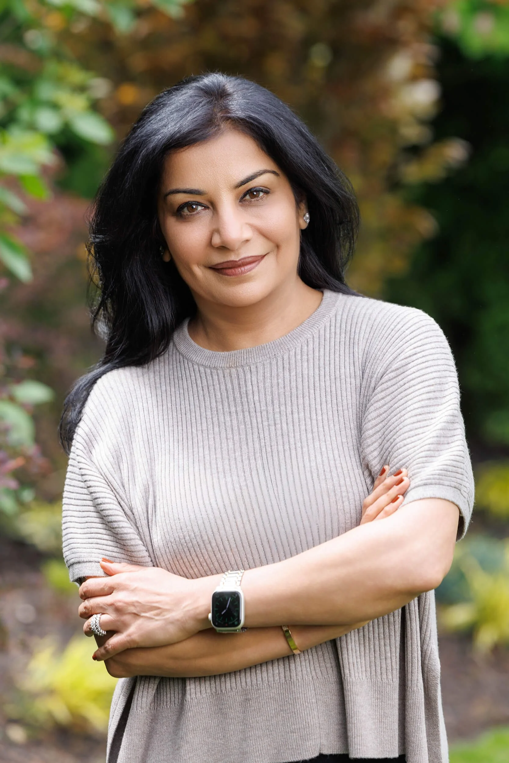 Dr. Anu Gupta, a physician specializing in women's metabolic health & weight management, standing outdoors with green and brown blurred foliage in the background.
