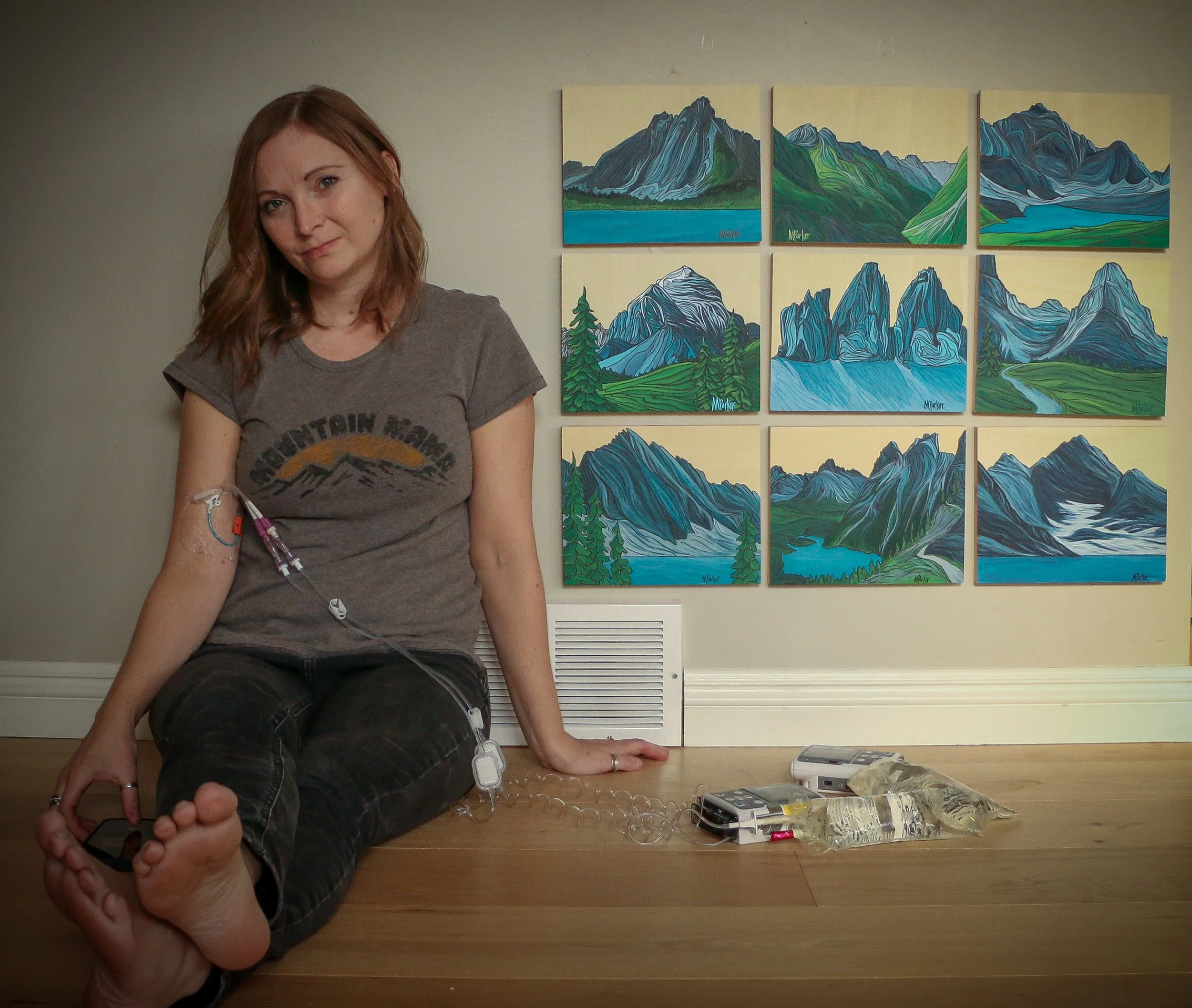 Minimalist landscape paintings of Canadian Rockies mountain ranges rendered in soft greens and blues on a natural wood panel, part of Megan Parker’s “Peaks and Valleys” series exploring chronic illness and healing.