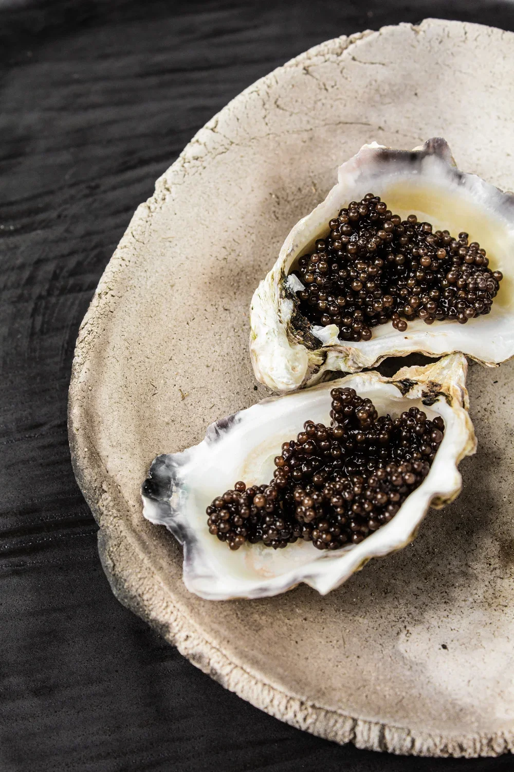 Two oyster shells filled with glossy black caviar on a rustic ceramic plate