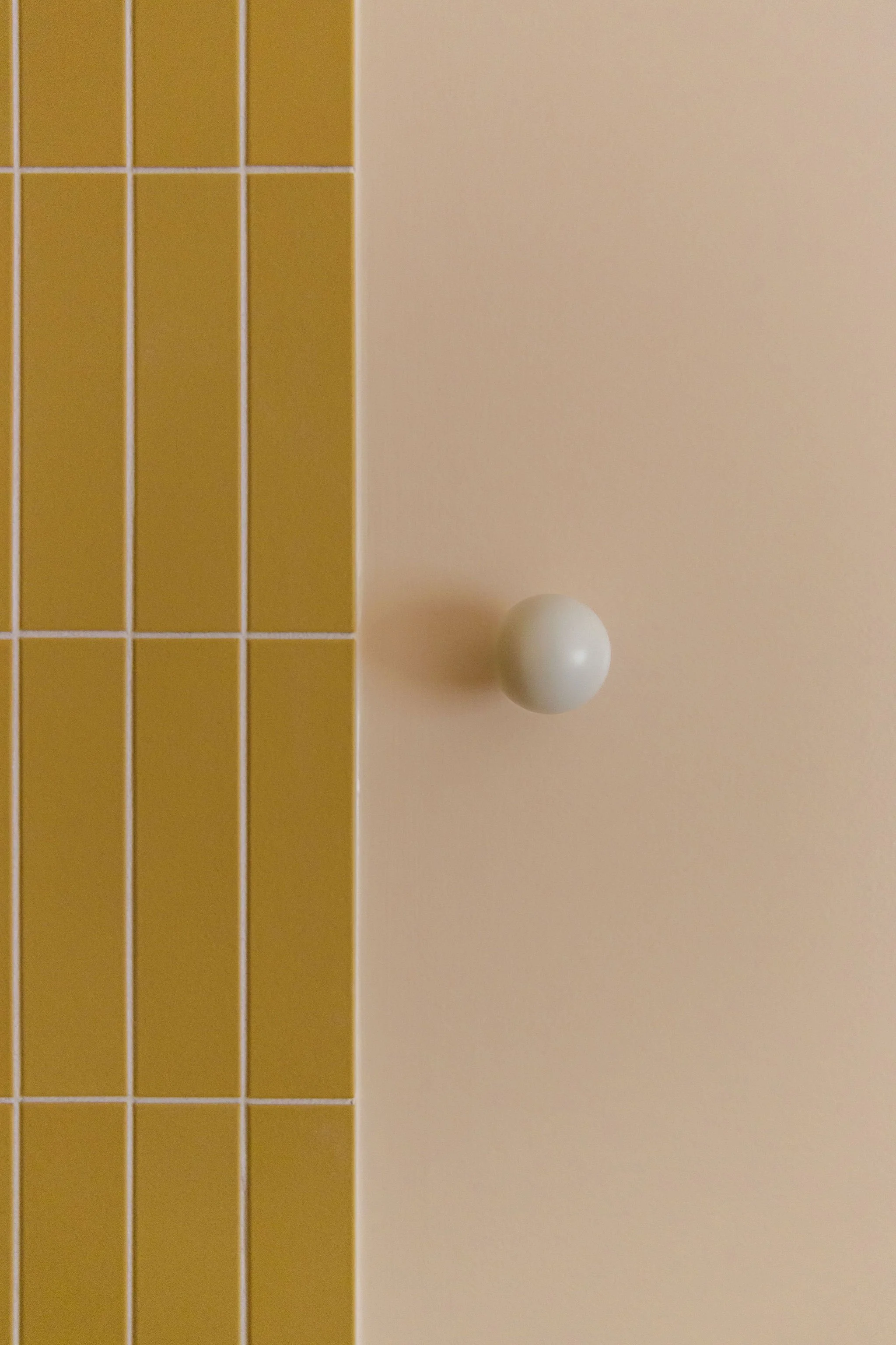 Close-up of a section of a yellow tiled wall and a pink wall with a small white towel hook.